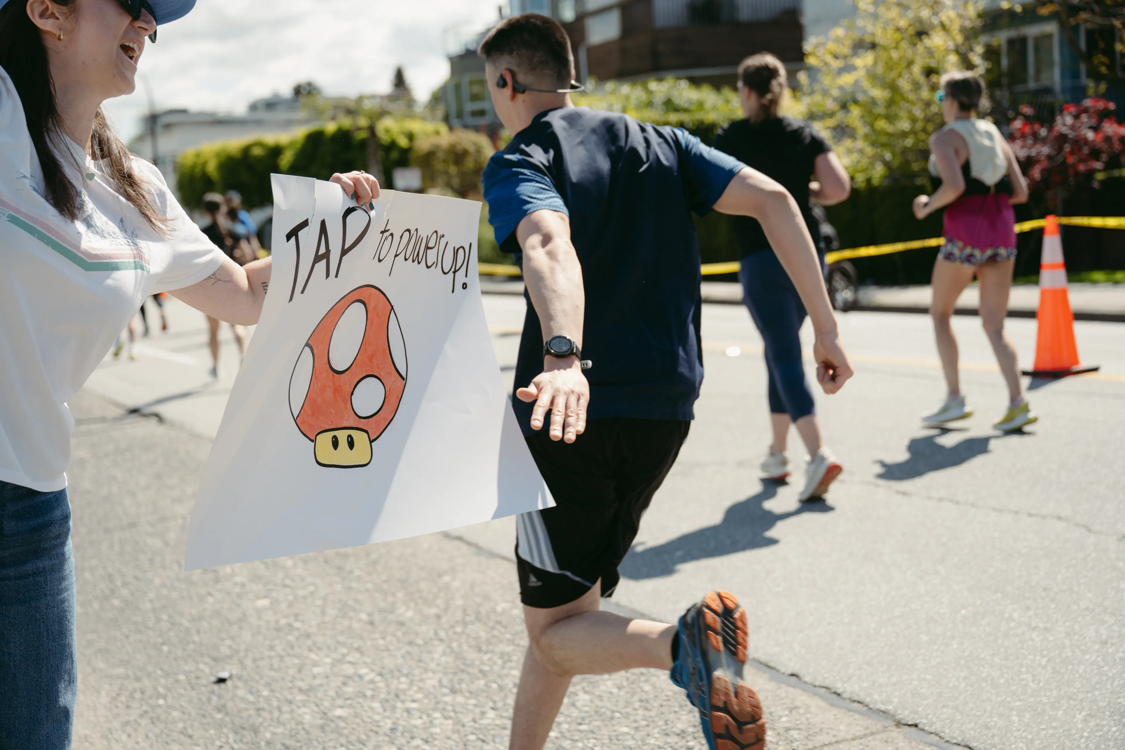 A runner tapping a sign that a spectator holds up that reads "Tap to power up" on the Sun Run in Vancouver.