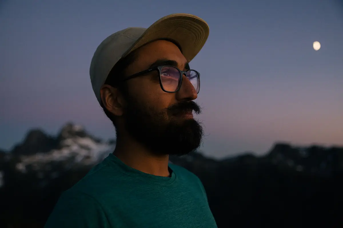 Trail runner JoJo Das stands atop a mountain at dusk.