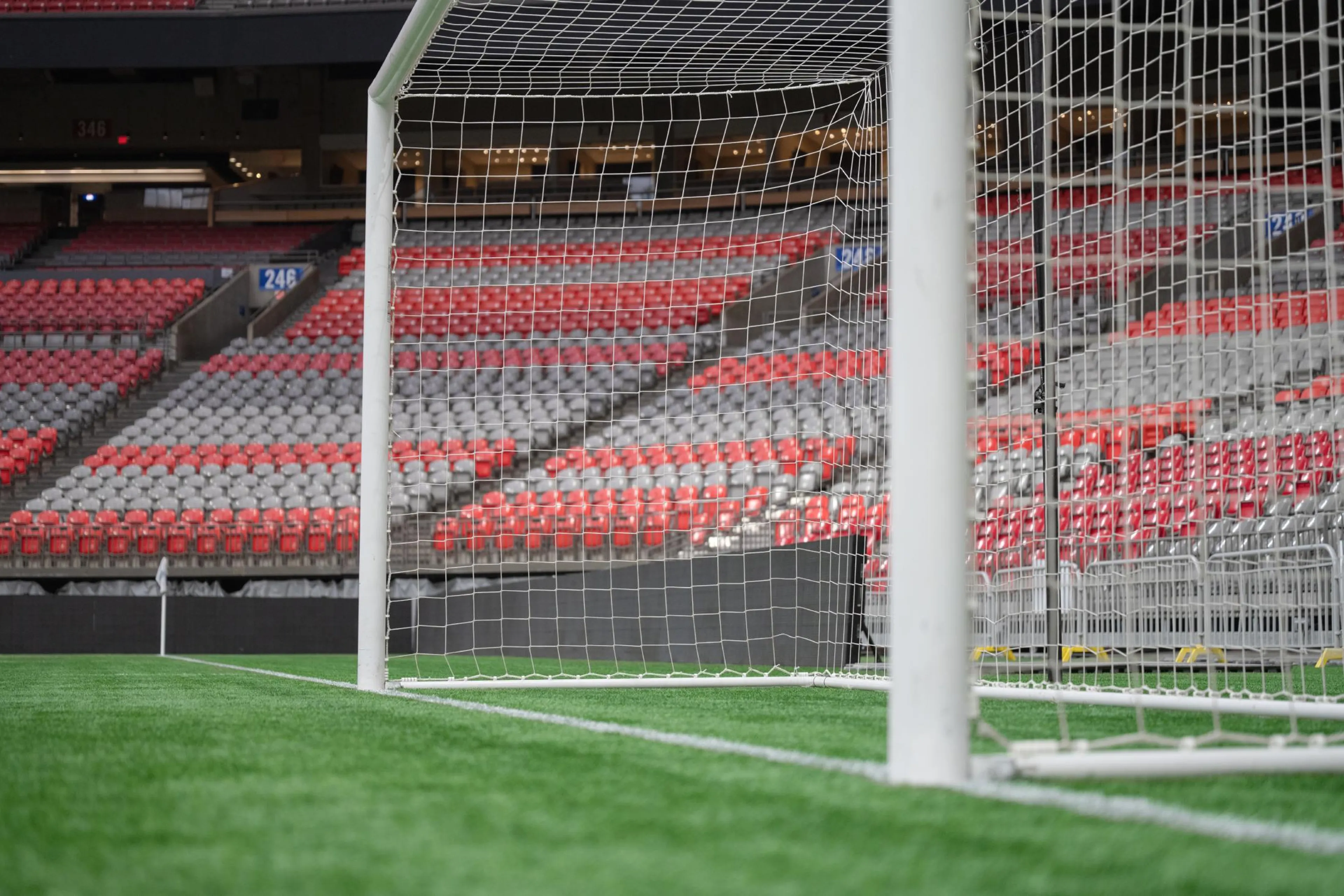 Empty soccer goal with net on a green field inside a stadium with red and gray seats.