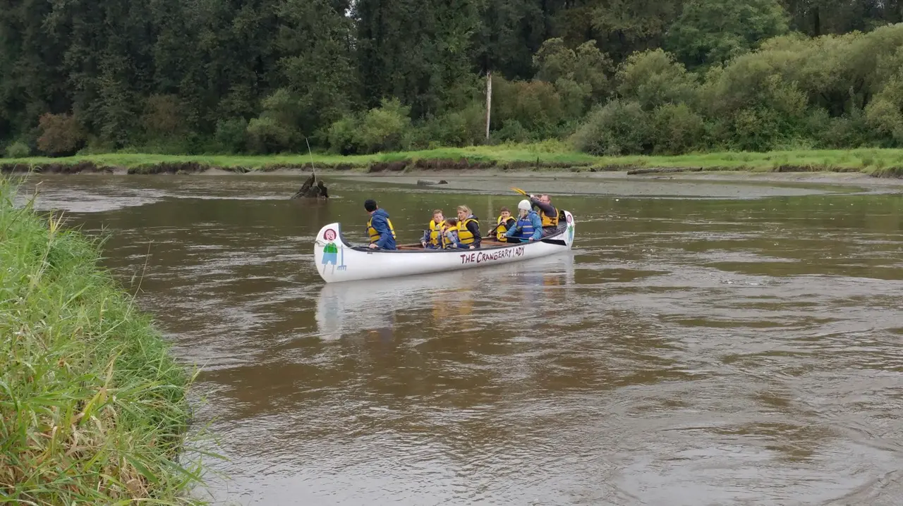 A group of adults and children paddles a canoe in Kanaka Creek