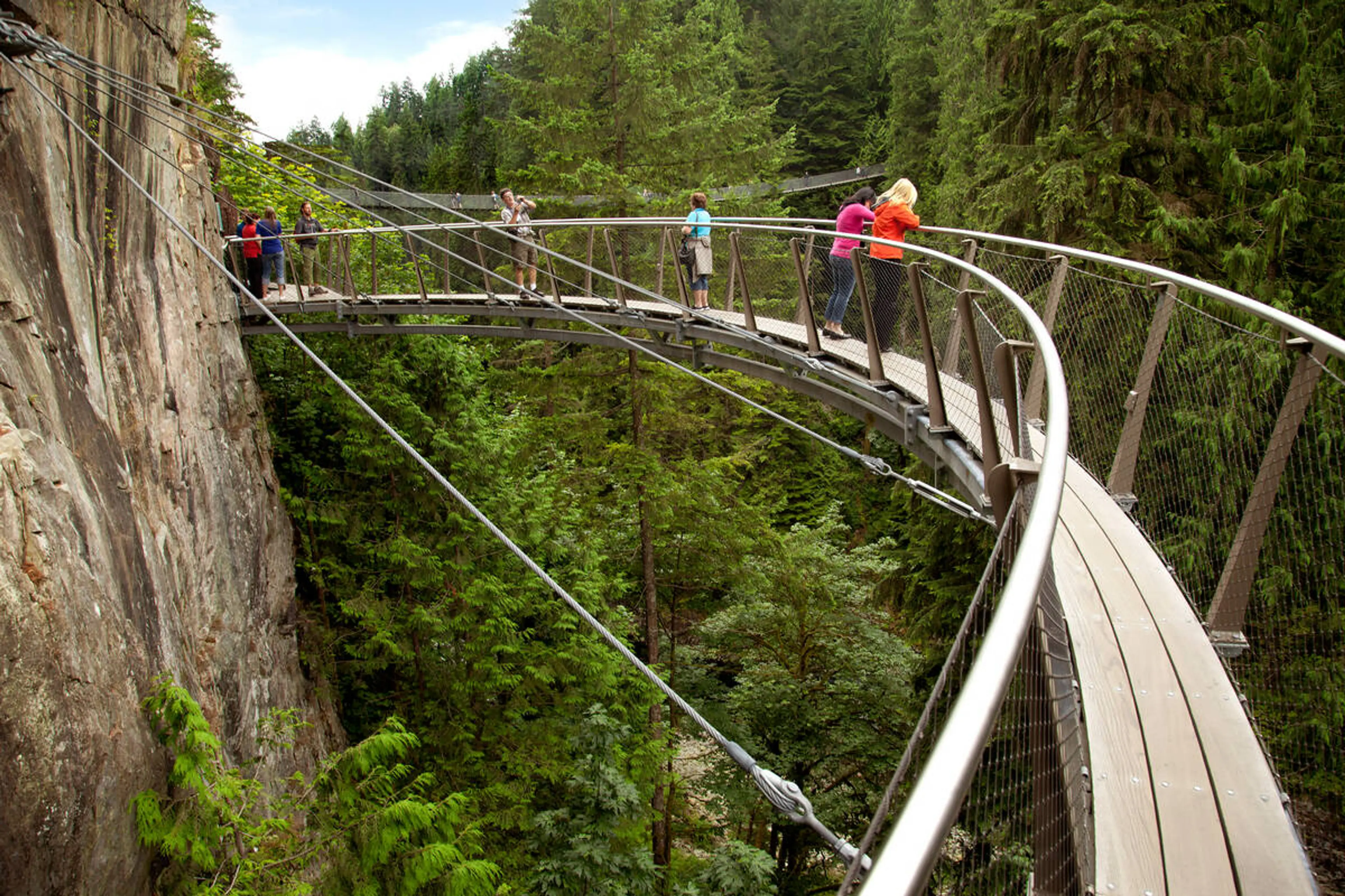 People stand on the cantilevered Cliffwalk at Capilano Suspension Bridge park. 