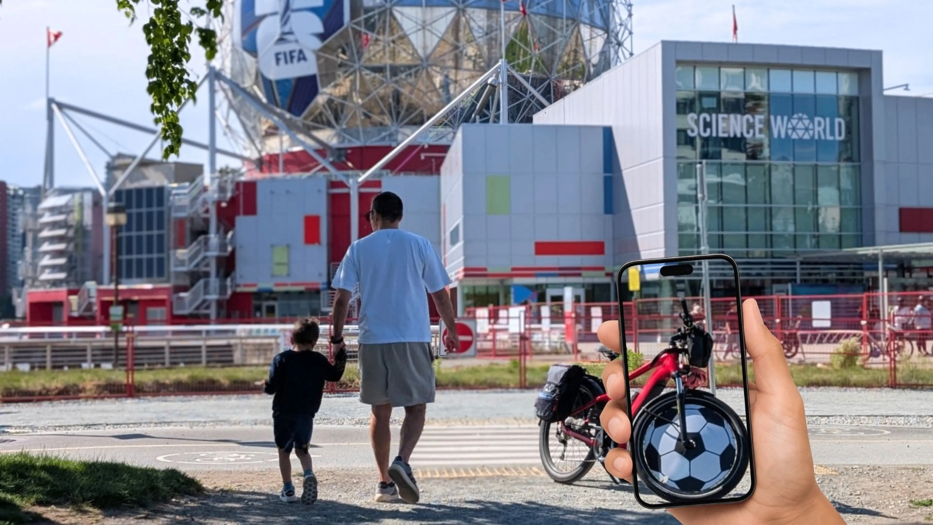 A person holding a phone showing a bicycle wheel designed like a soccer ball, with a person and child walking toward a building labeled Science World in the background.
