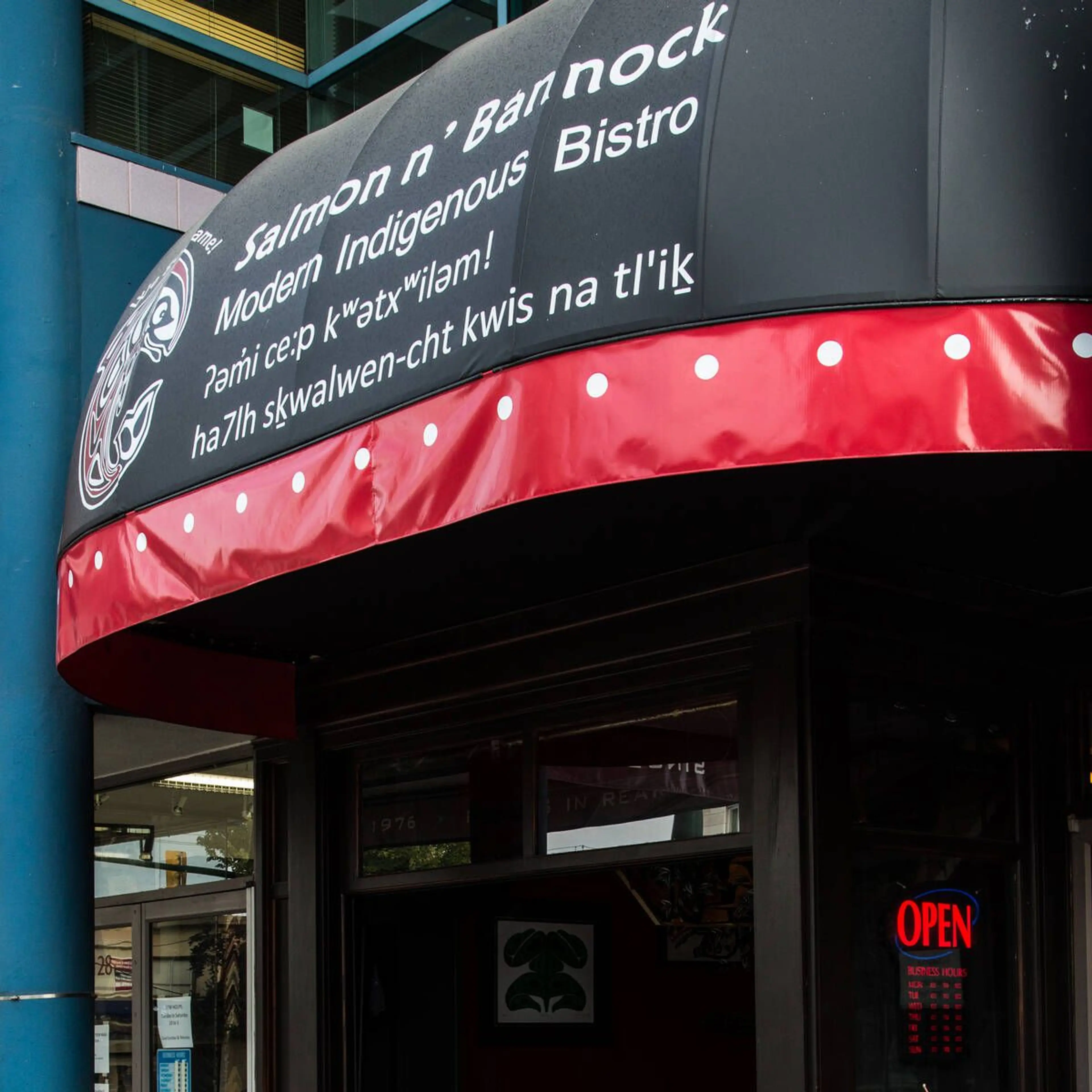 Black and red awning with white text reading Salmon n' Bannock Modern Indigenous Bistro above a restaurant entrance with an open sign.