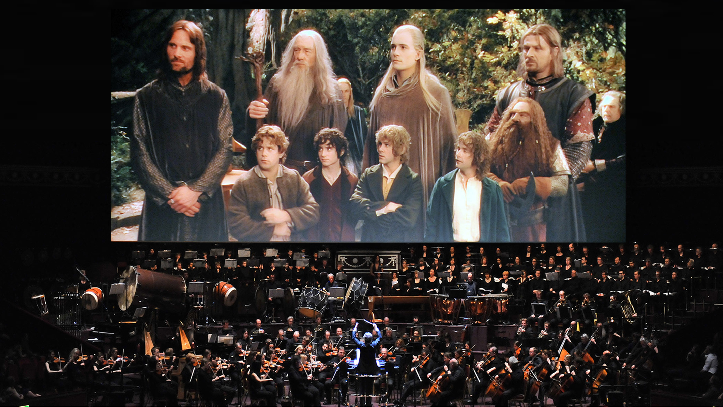Orchestra and choir performing live in front of a large screen showing a scene from The Lord of the Rings with characters standing in a forest.