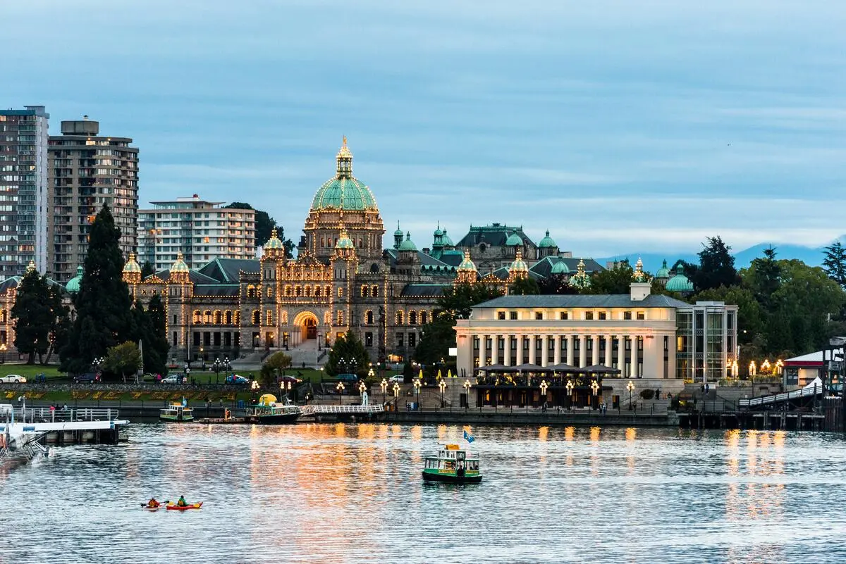 A scenic view of the Inner Harbour at night, with the Parliament Buildings lit up, boats in the marina, and two kayakers enjoying an evening paddle.