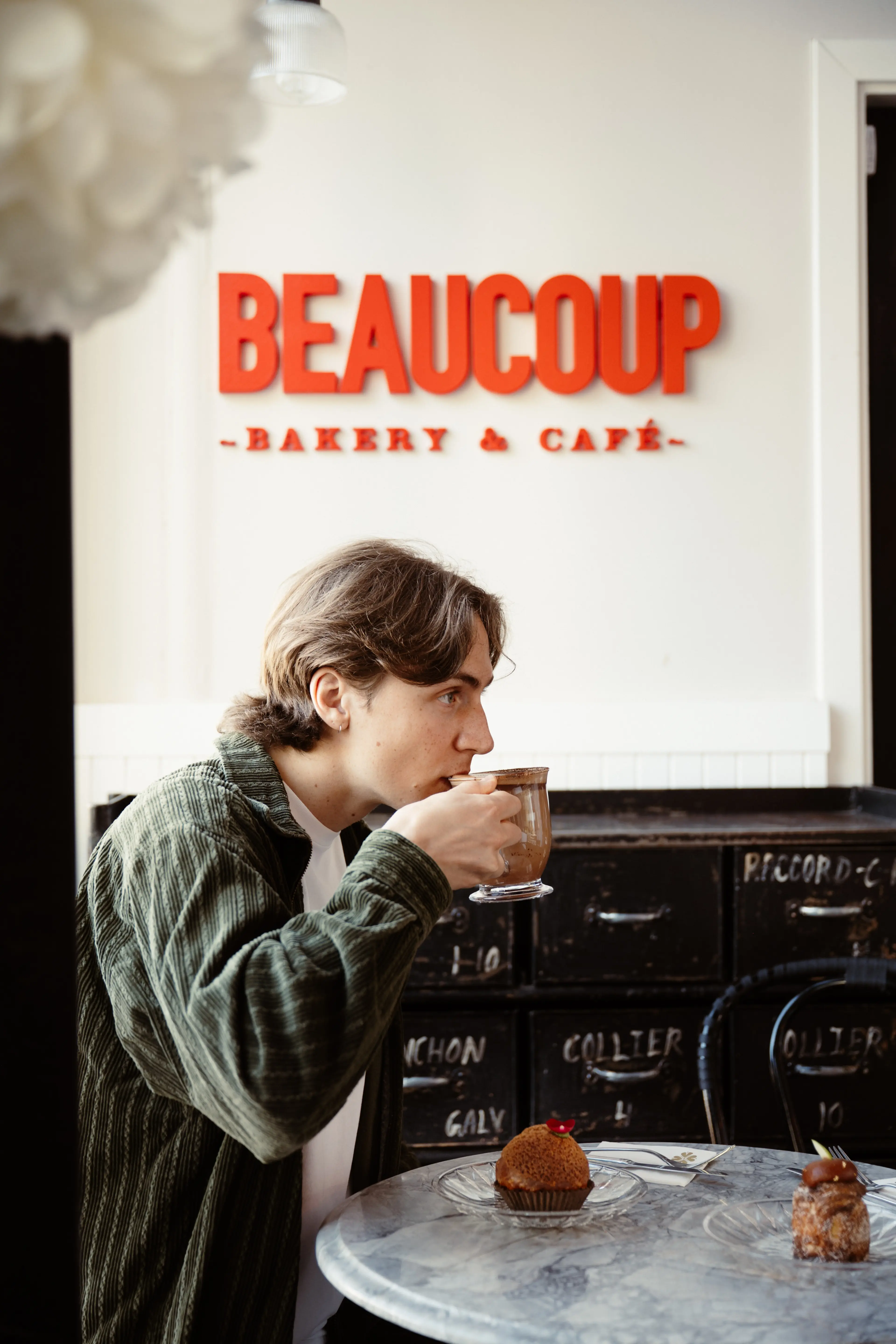 A person sitting in the Beaucoup Bakery and Café holding up a mug.