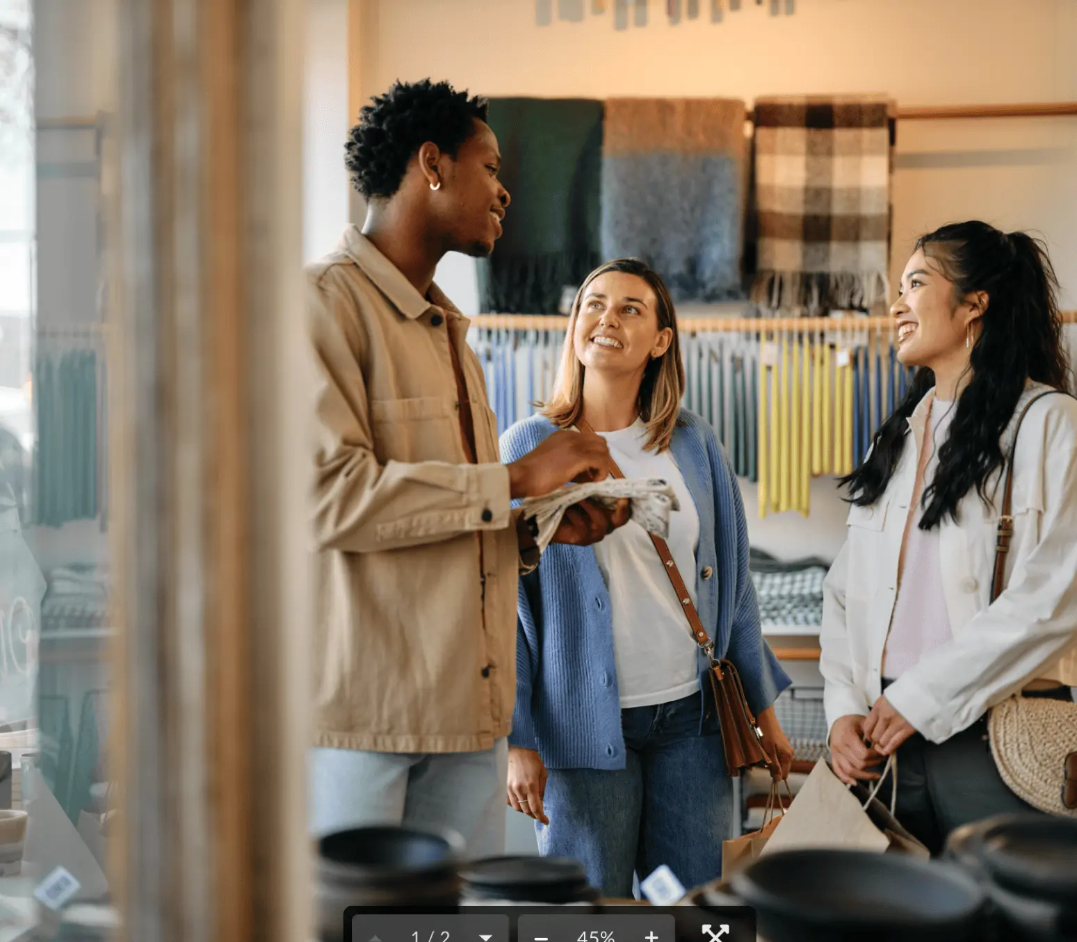 Three people smiling and talking inside a store with scarves and fabrics displayed on the wall behind them.