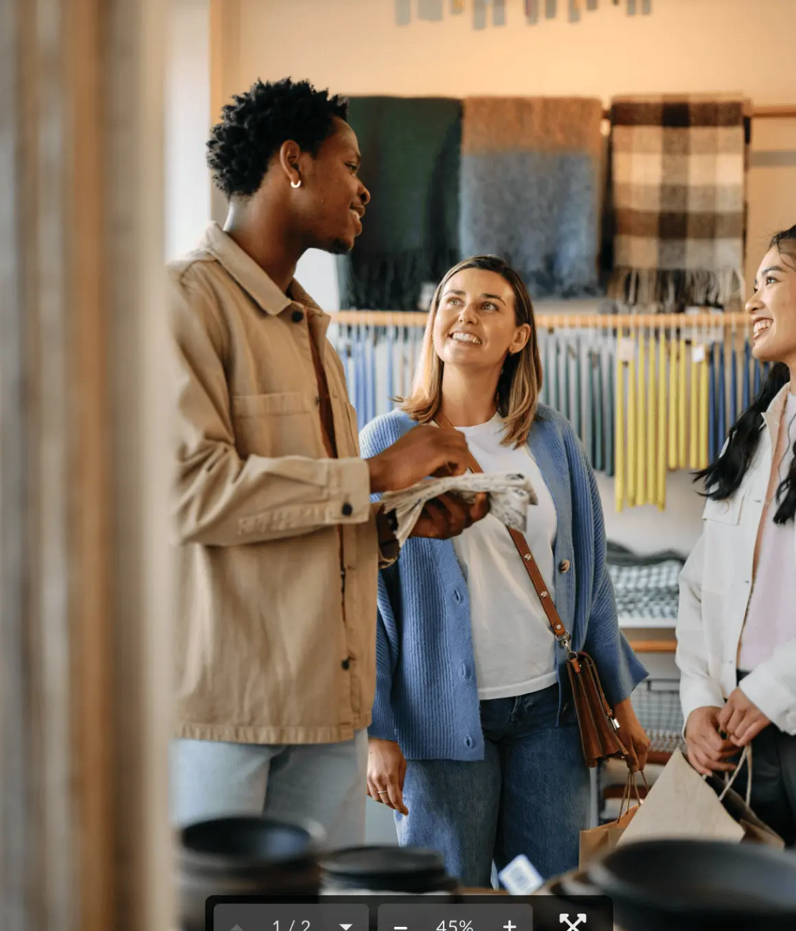 Three people smiling and talking inside a store with scarves and fabrics displayed on the wall behind them.
