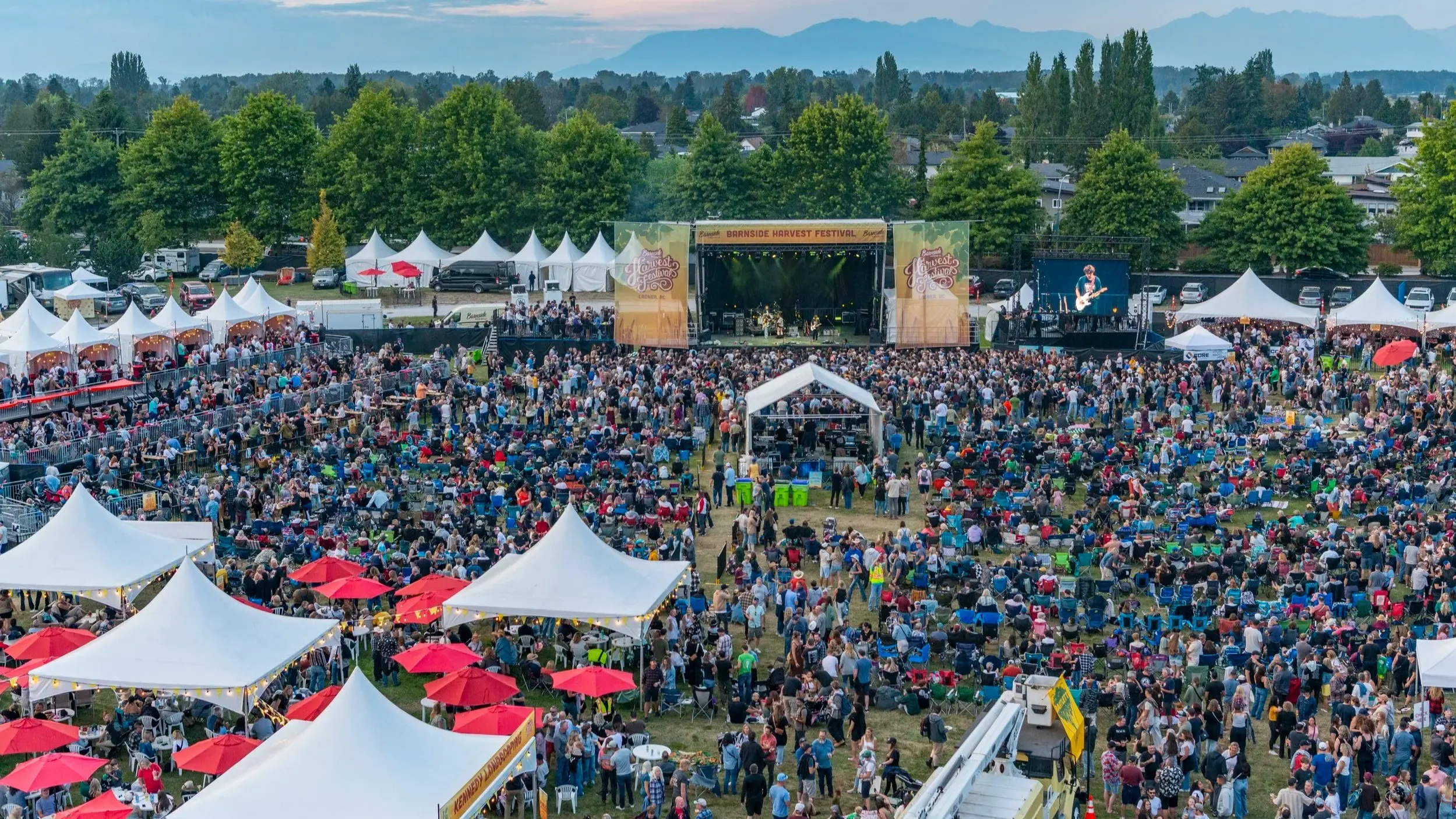 Large outdoor music festival crowd with white tents, red umbrellas, and a stage with a band performing.