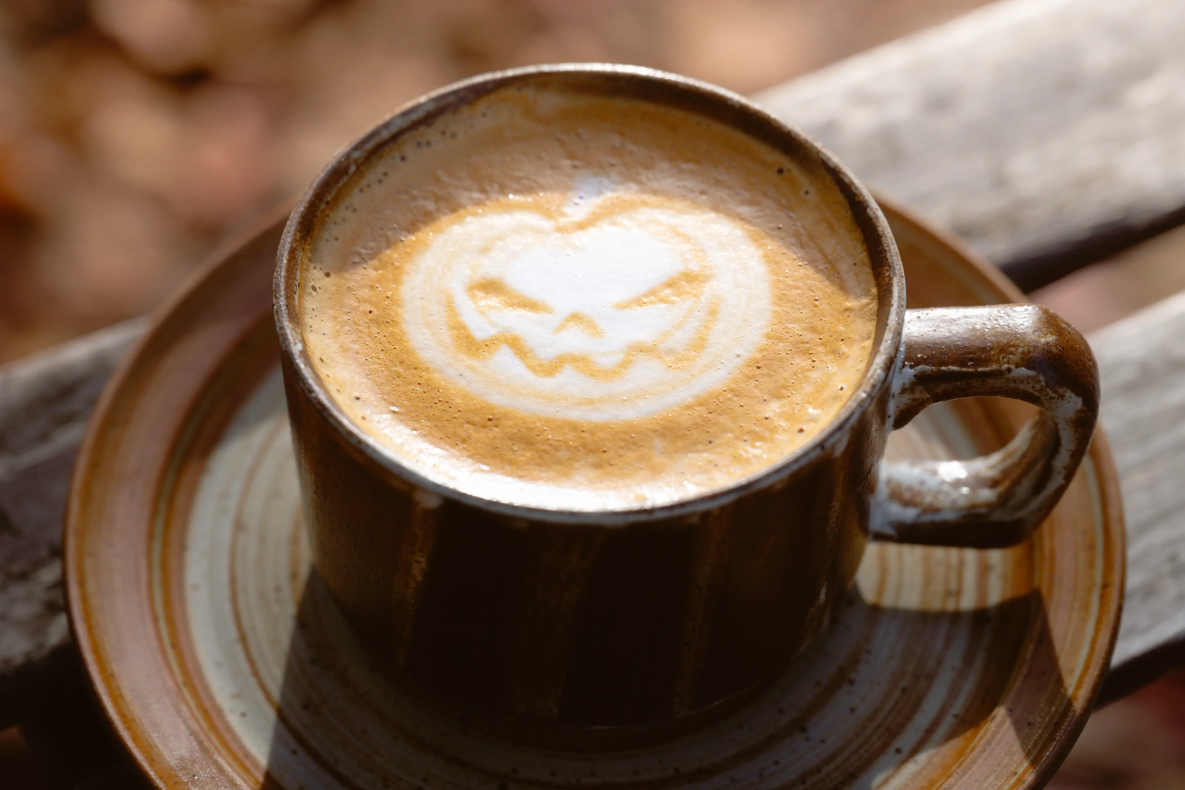 A coffee mug on a bench with a pumpkin design drawn into the foam.