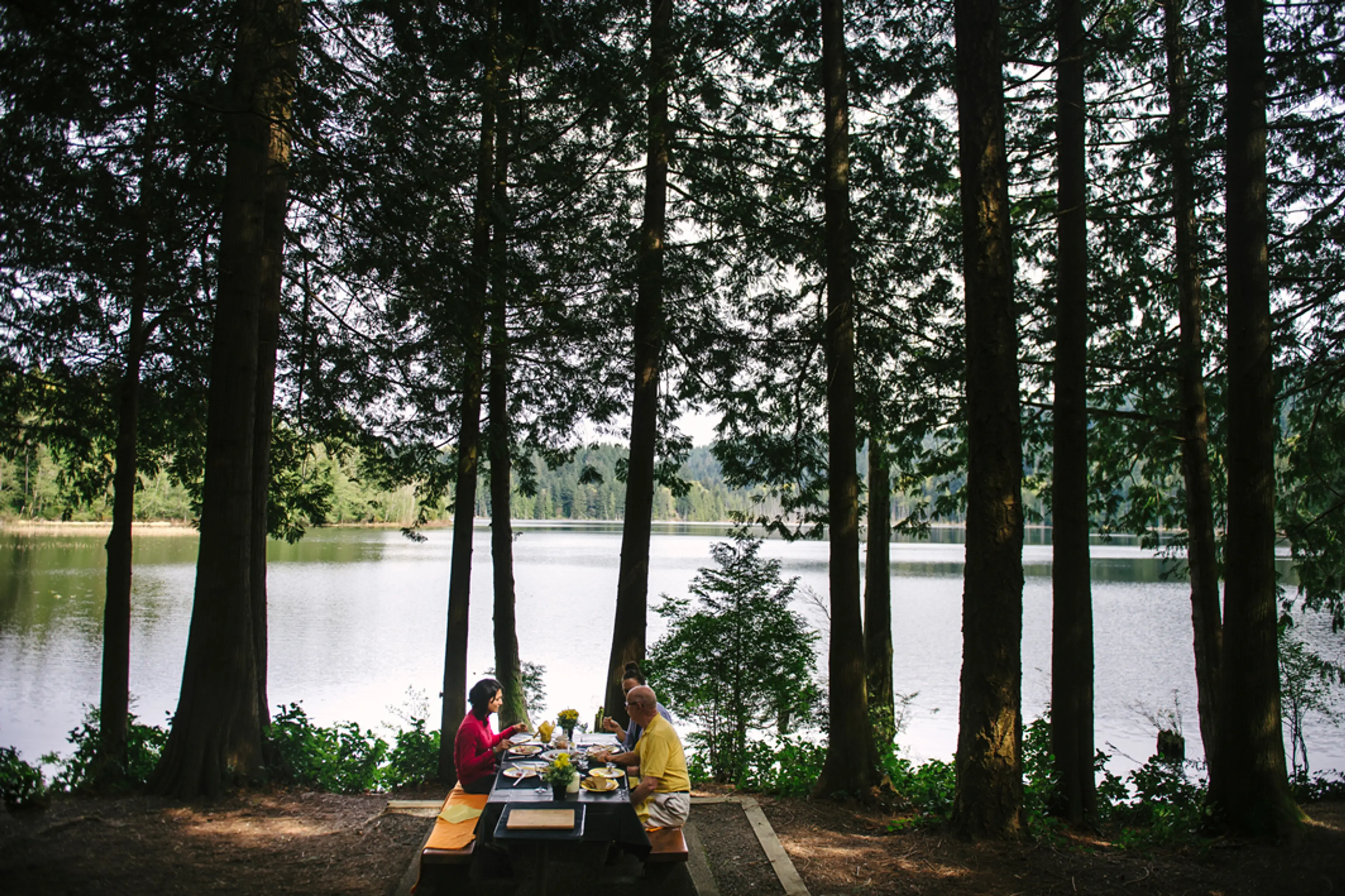 People eating at a picnic table besides Killarney Lake on Bowen Island near Vancouver, BC