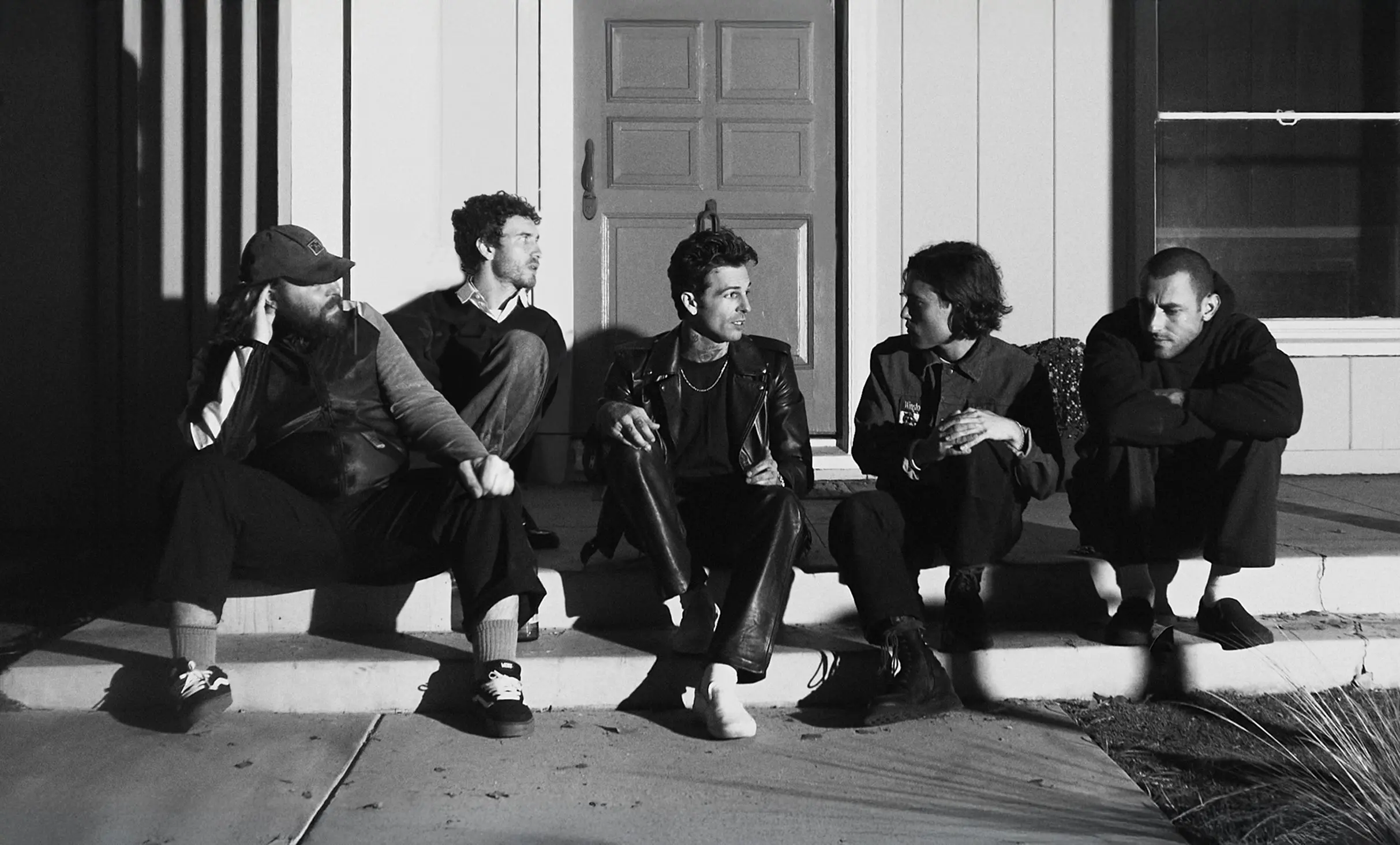 Five people sitting on outdoor steps in front of a door, engaged in conversation, in black and white.