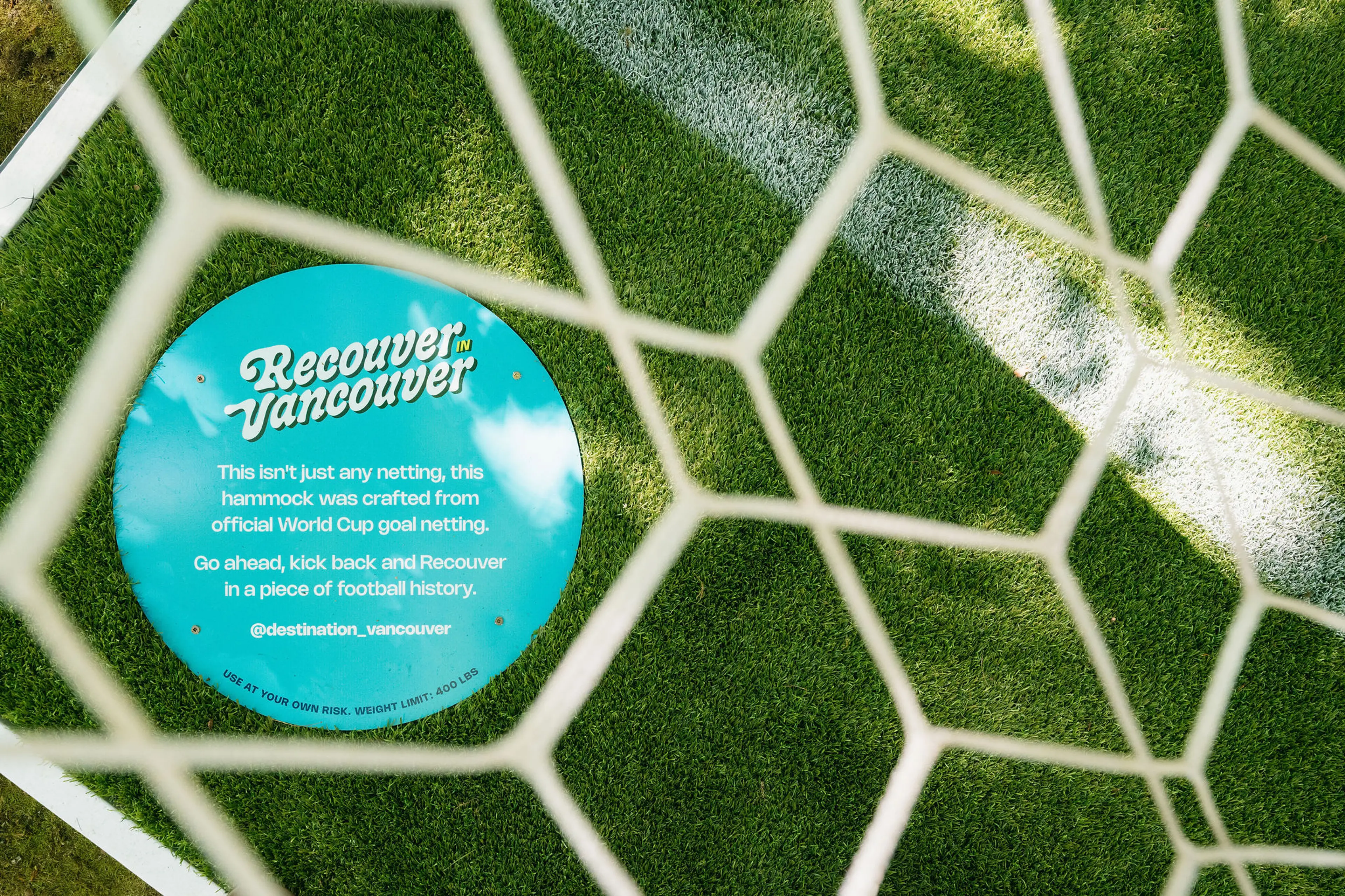 Blue circular sign on green grass behind white soccer goal netting with text about hammock made from official World Cup goal netting.