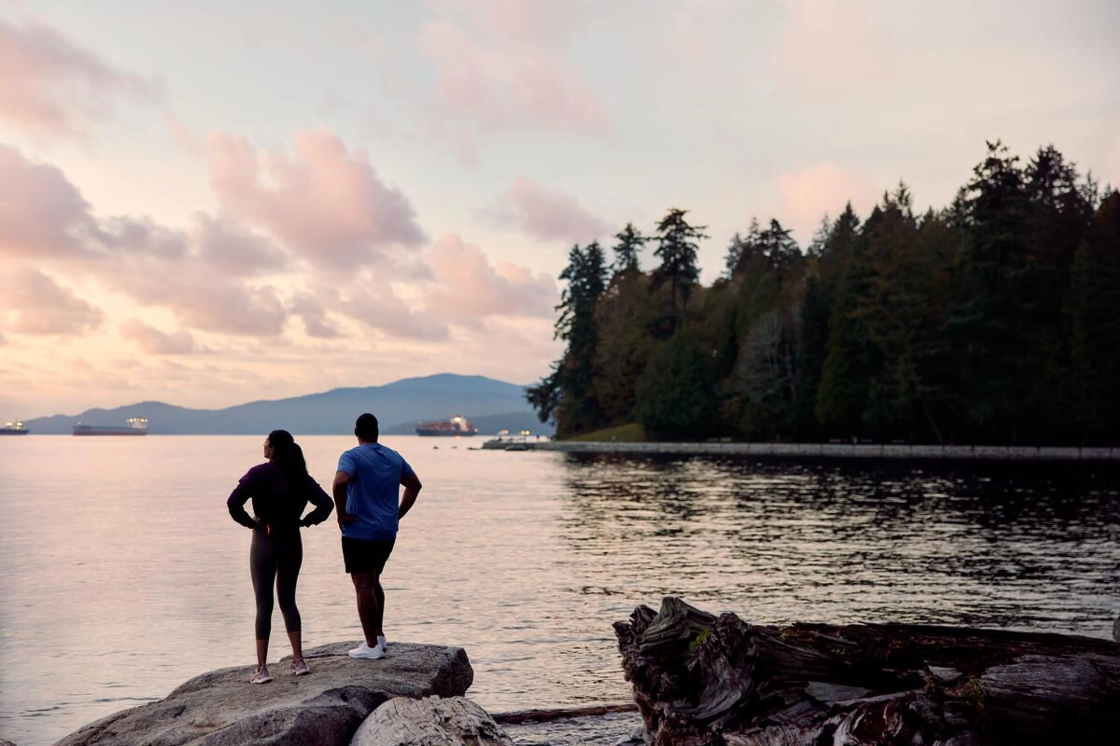 Two people looking out on the ocean to see the sunset at Stanley Park in Vancouver.