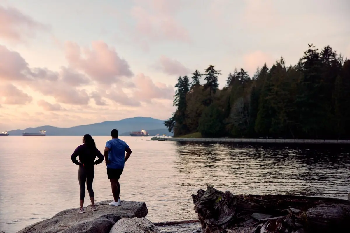 Two people looking out on the ocean to see the sunset at Stanley Park in Vancouver.