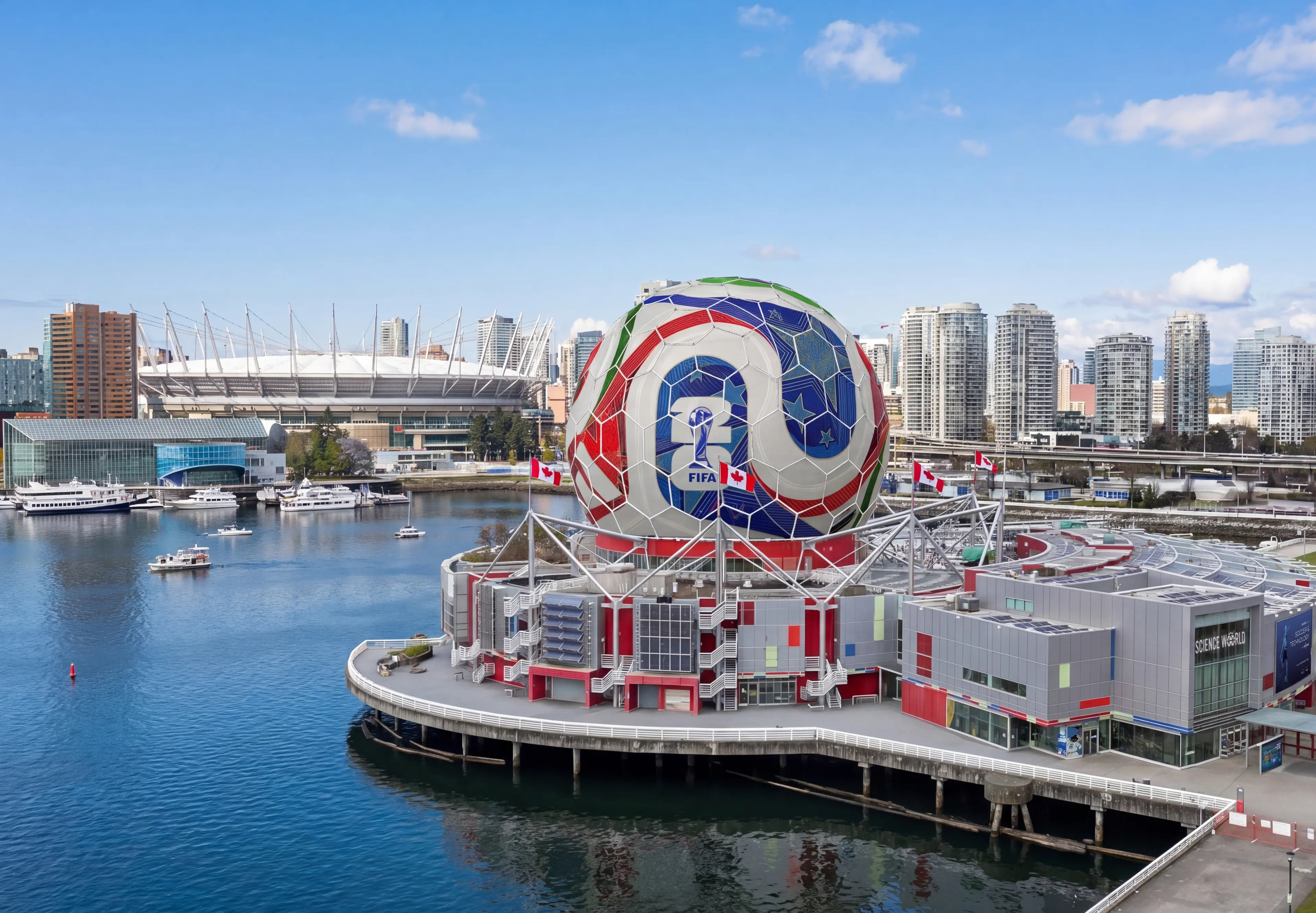 Large spherical structure decorated like a soccer ball with FIFA logo on a waterfront building, city skyline in background.
