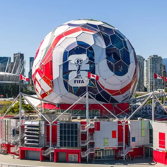 Large spherical building painted like a soccer ball with FIFA logo, surrounded by water and city skyline in the background.