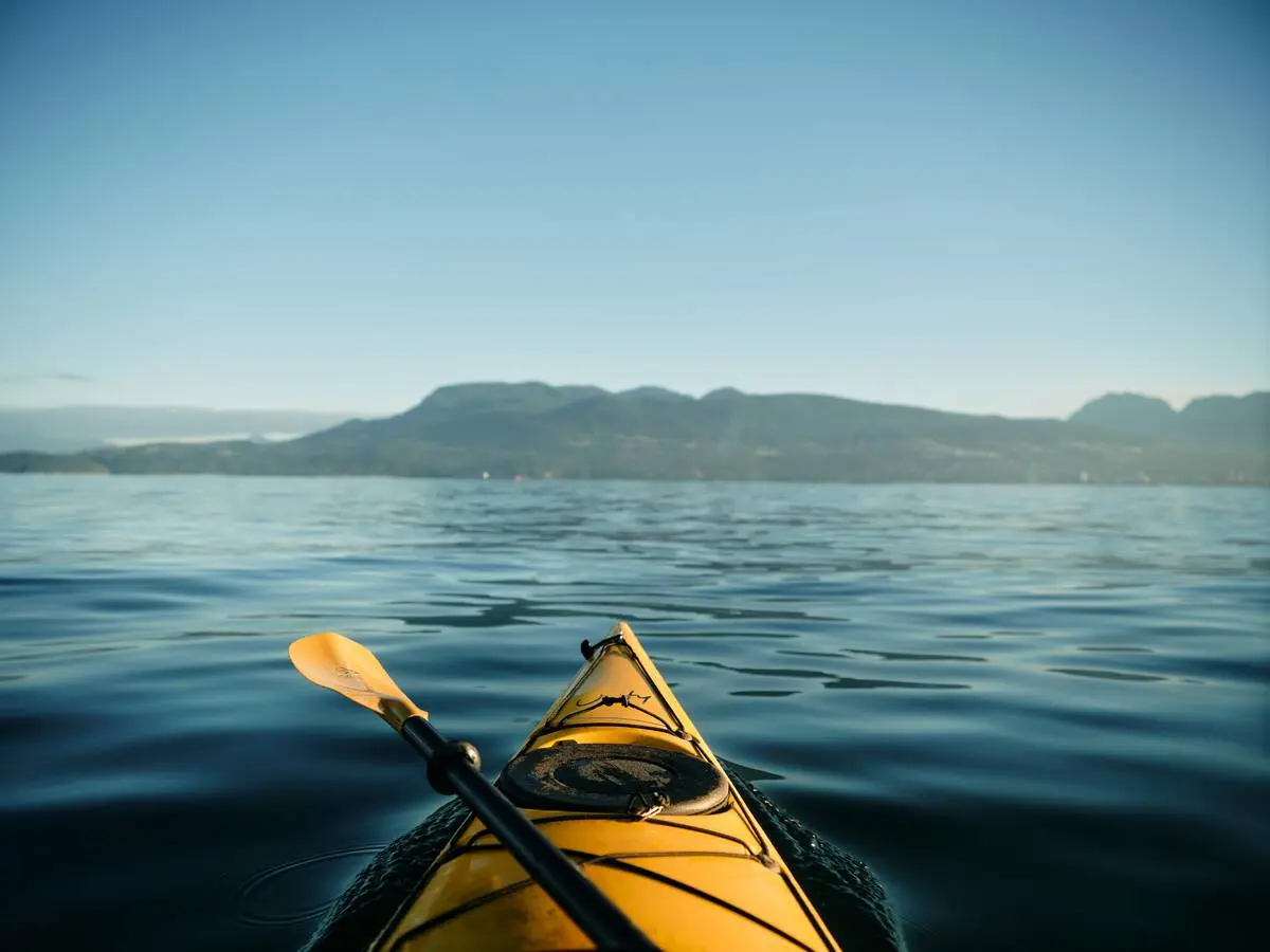 A tip of a canoe on calm waters with mountains in the distance in Deep Cove, North Vancouver.