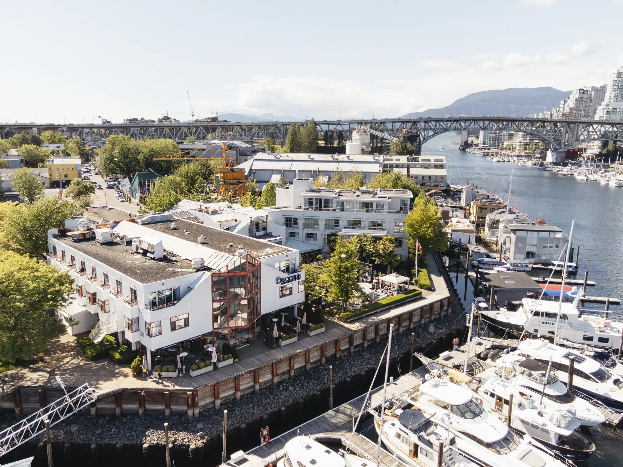 An aerial view of Granville Island with hotels along the pier and yachts docked outside.