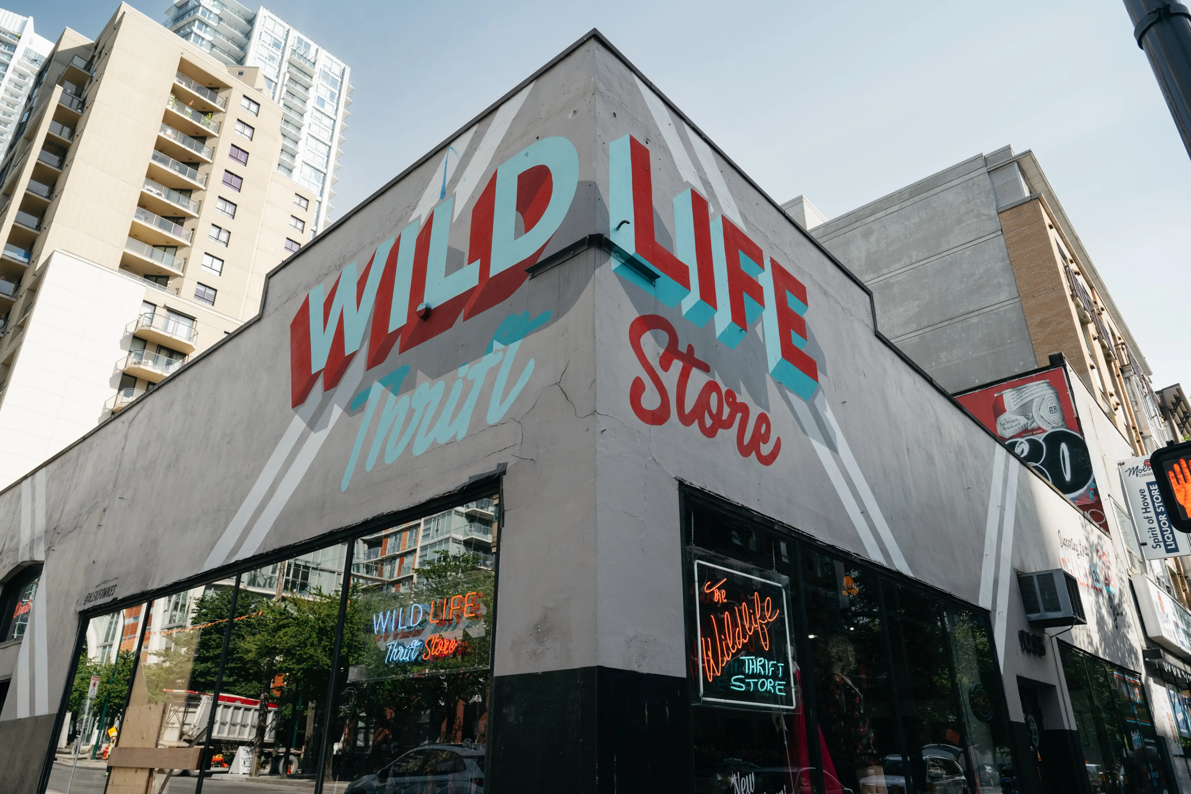 The exterior of the Wildlife Thrift Store in Vancouver. It includes a brightly painted mural-style sign and a vintage-looking neon sign in the window. 