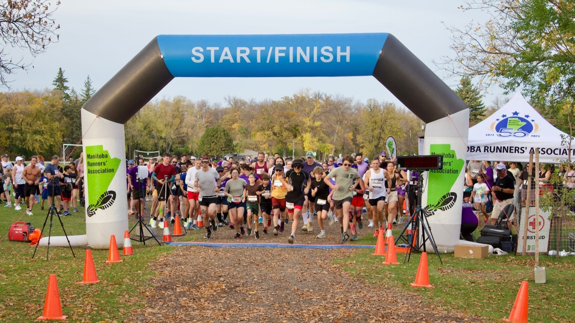 A group of runners starting a race under a blue and white inflatable arch labeled START/FINISH with orange cones lining the path.