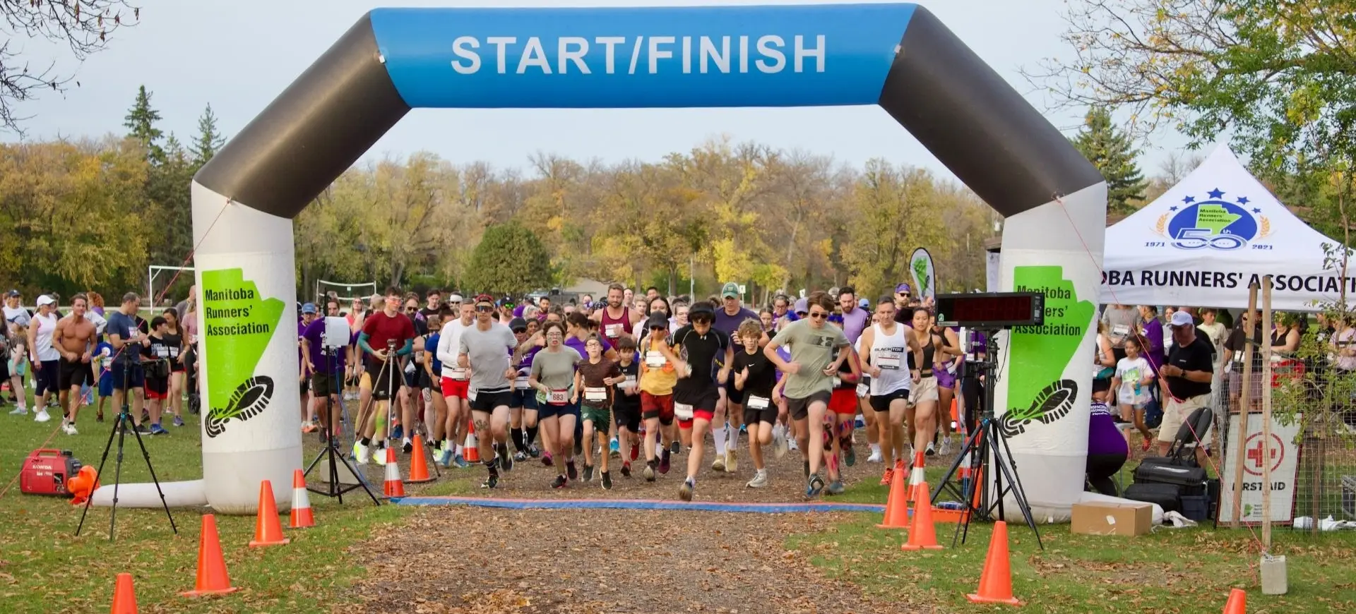 A group of runners starting a race under a blue and white inflatable arch labeled START/FINISH with orange cones lining the path.