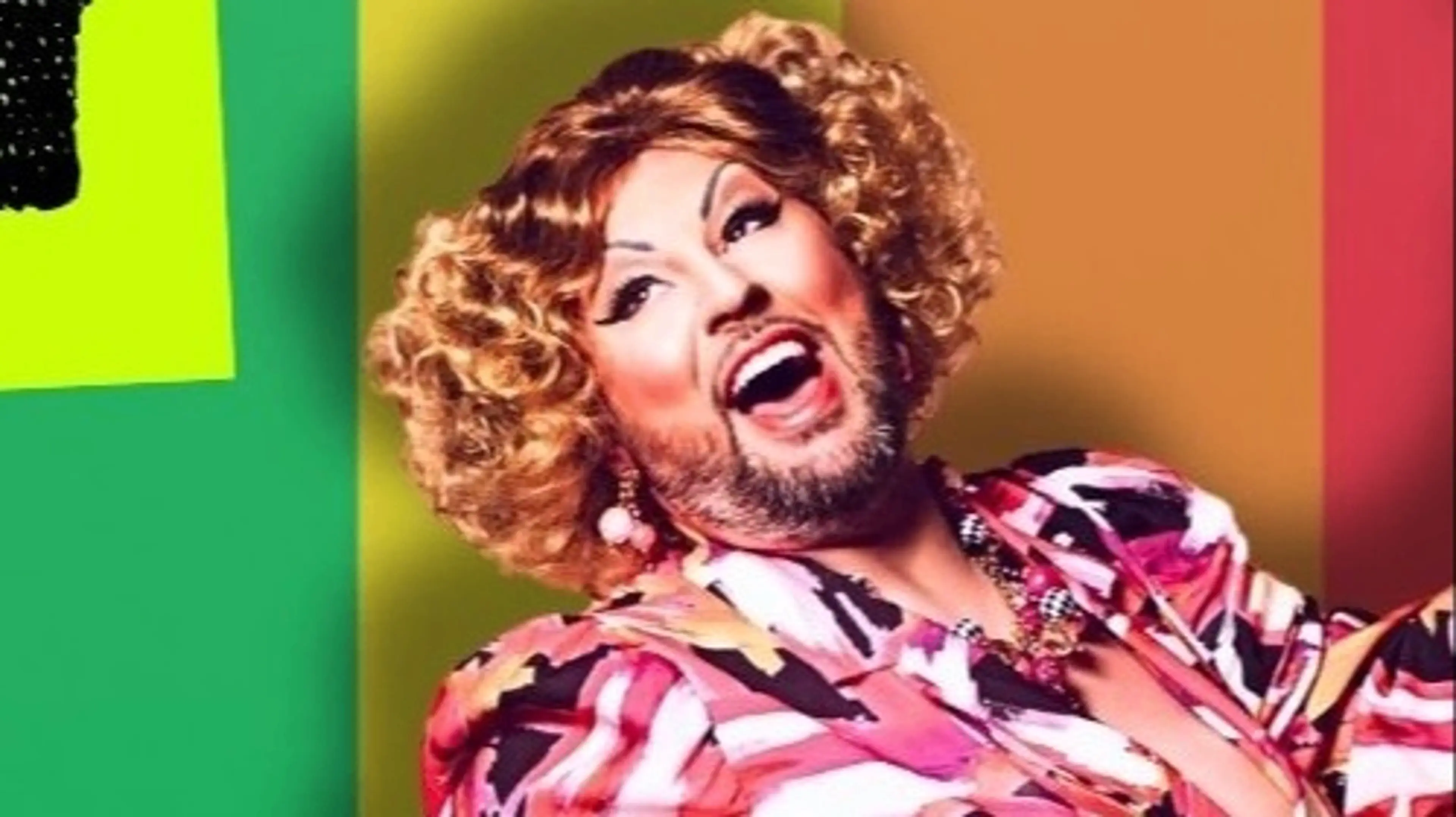 Person with curly hair and beard wearing colorful patterned clothing, smiling widely against a multicolored background.