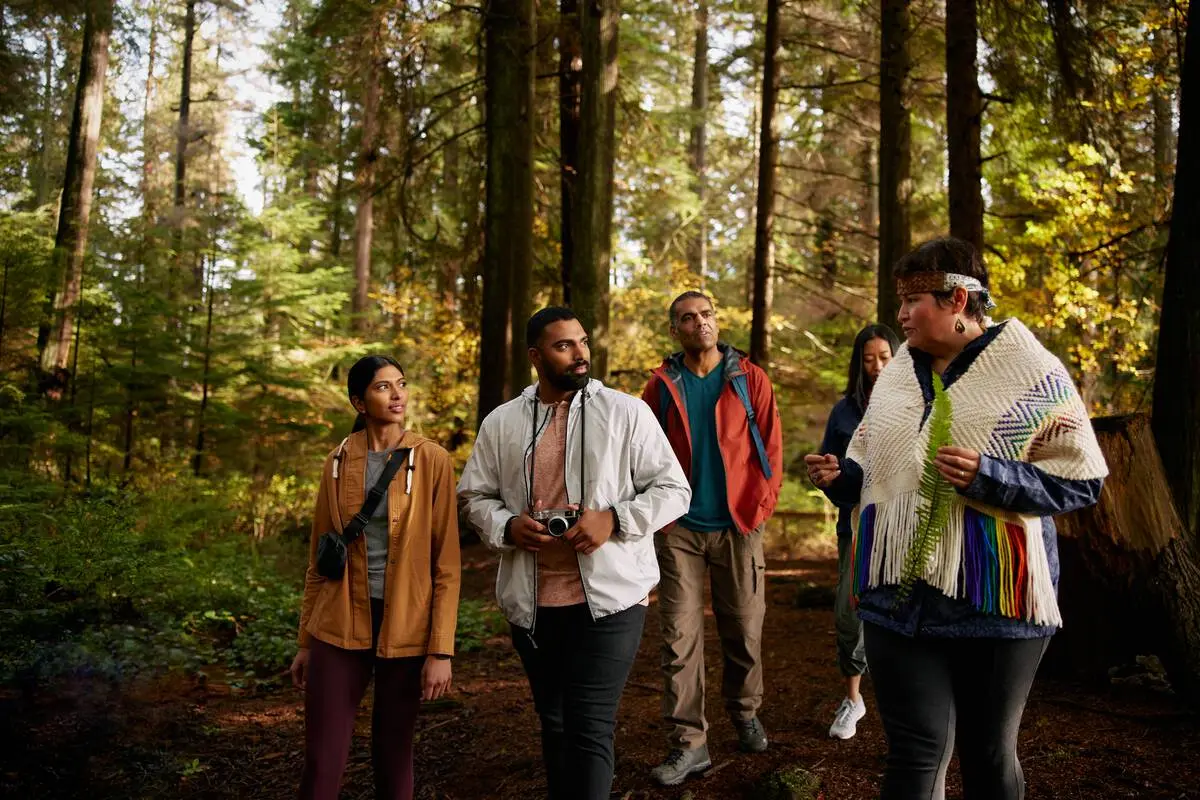 Candace Campo from Talaysay Walking Indigenous Tours is conducting a presentation and speaking to a group while on a walking experience in Stanley Park in Vancouver.