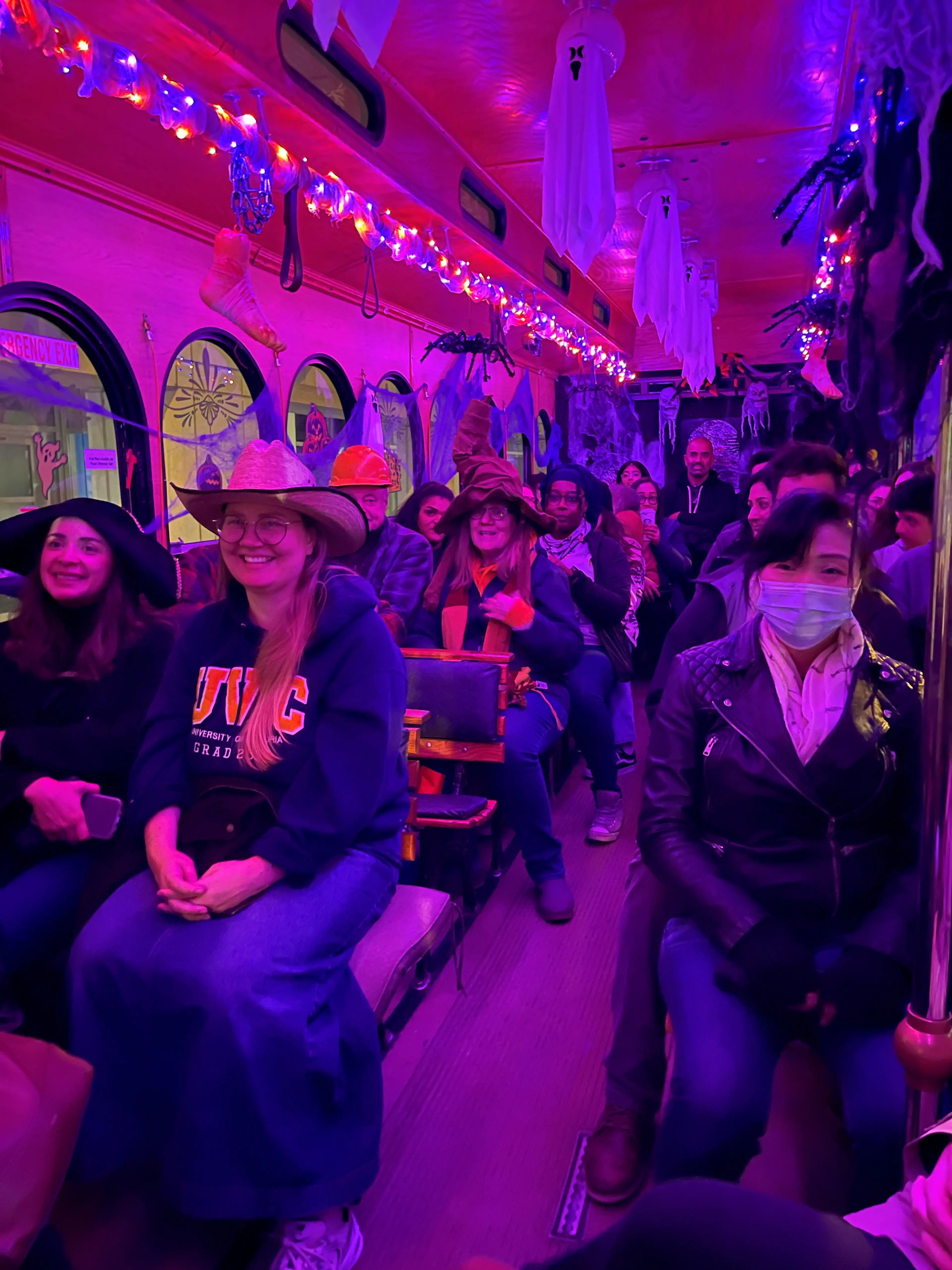 People sitting inside a bus decorated with Halloween lights, hanging ghosts, spiders, and other spooky decorations.