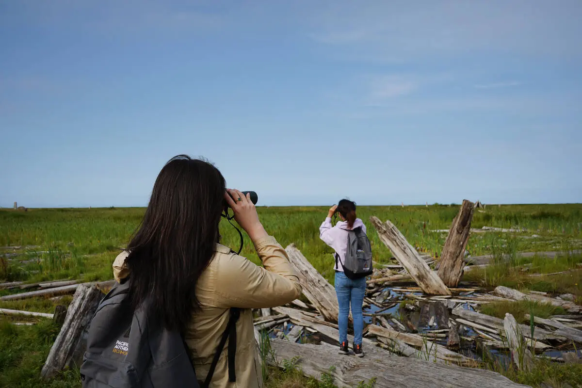 Two women stand with their backs to the camera watching birds at Terra Nova Rural Park in Richmond, part of the BC Bird Trail