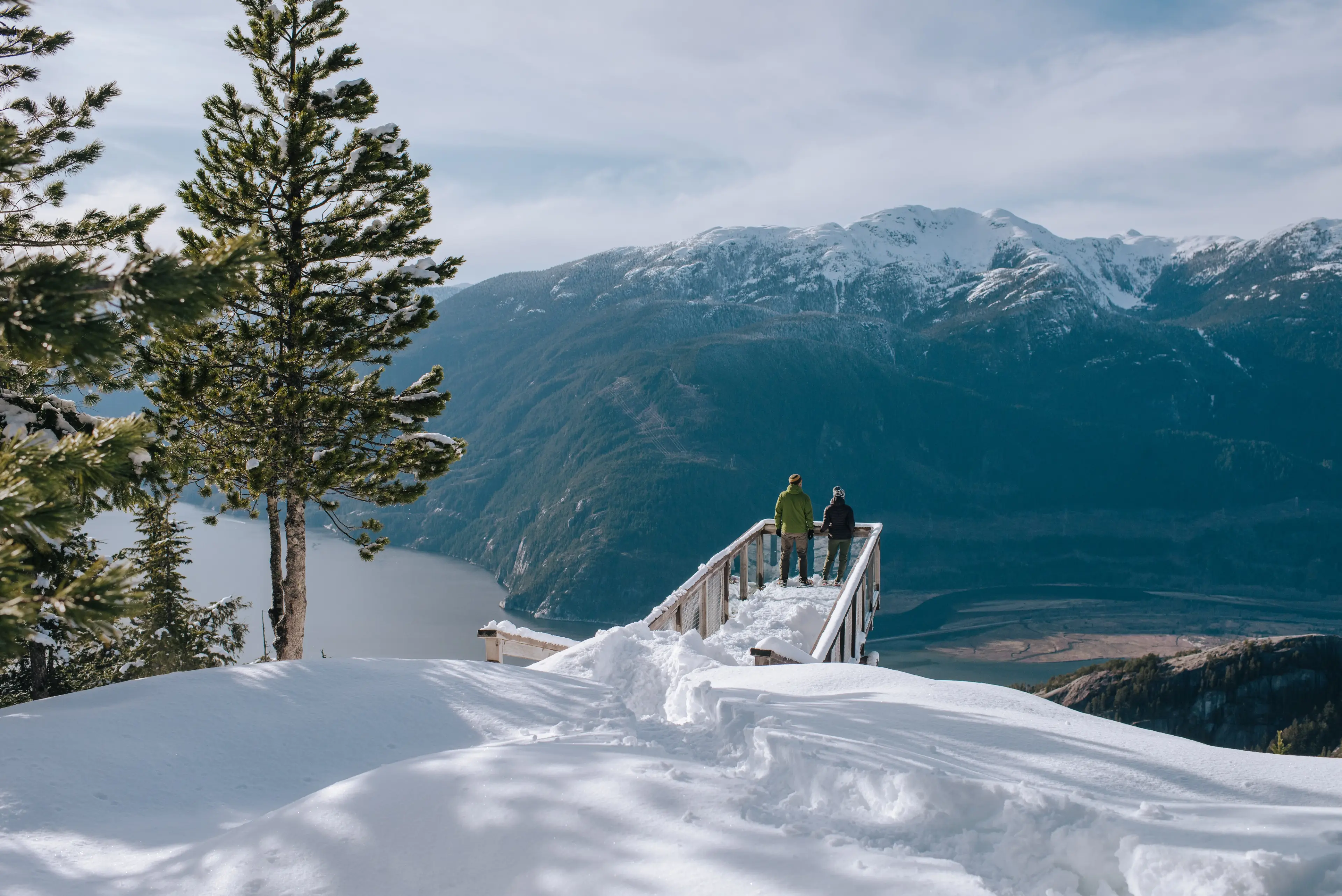 Two hikers stand on a viewing platform at the Sea to Sky Gondola in winter. 
