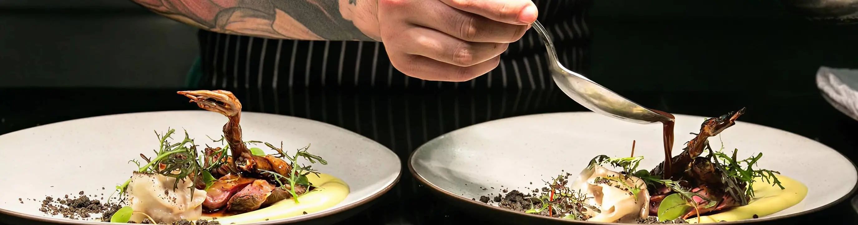 a chef with tattoo on his arm pouring sauce on a nicely plated dish