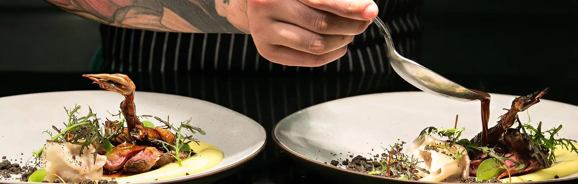 a chef with tattoo on his arm pouring sauce on a nicely plated dish