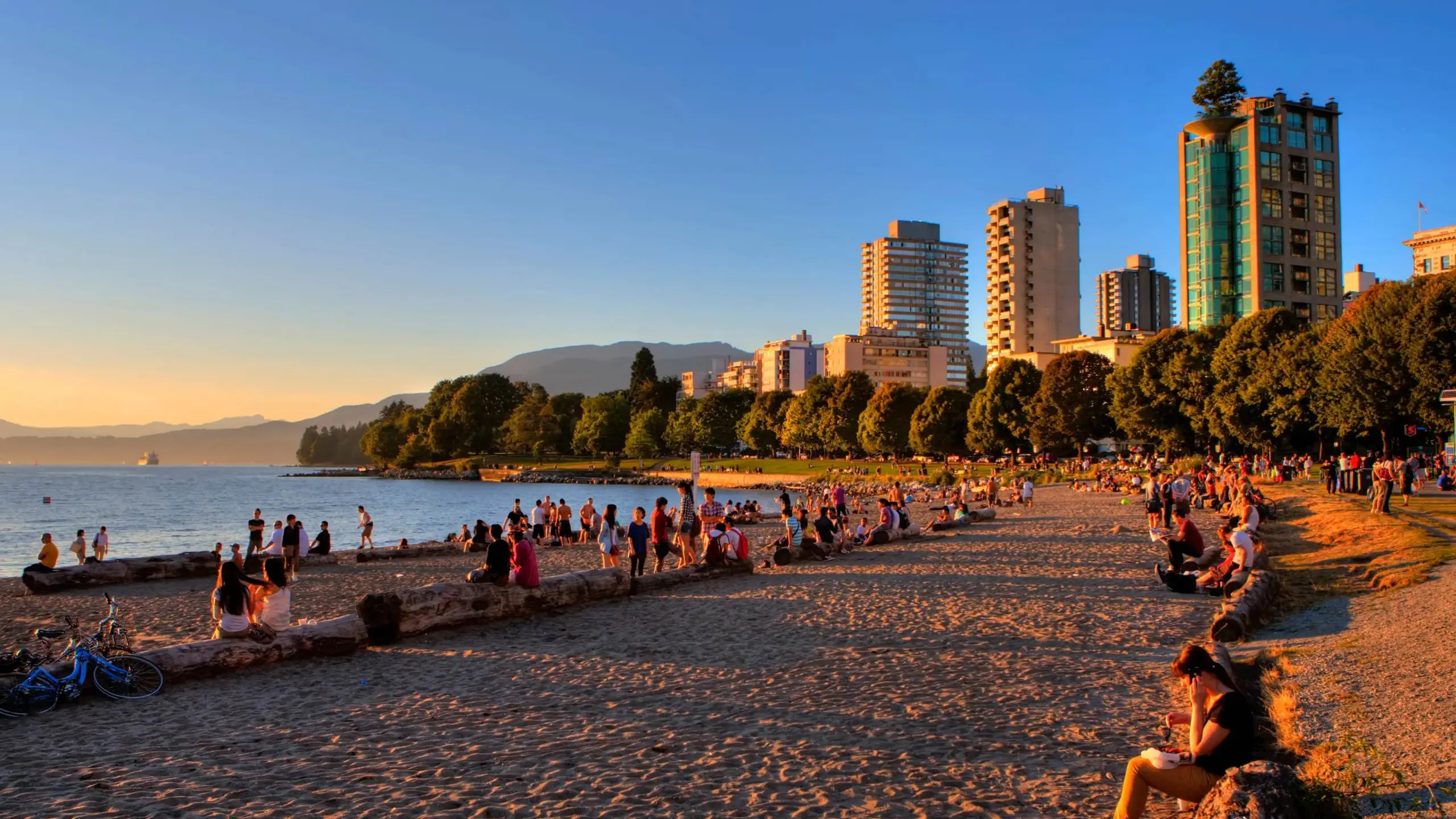 A wide-angle, golden-hour shot of English Bay Beach in Vancouver during a vibrant sunset.