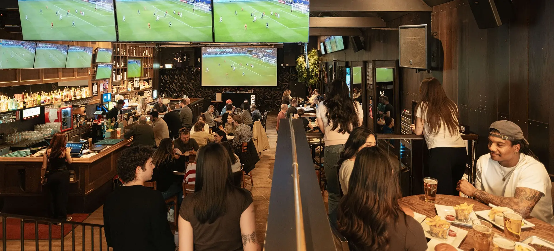 Crowded sports bar with people sitting at tables and bar, multiple TVs showing a soccer game.
