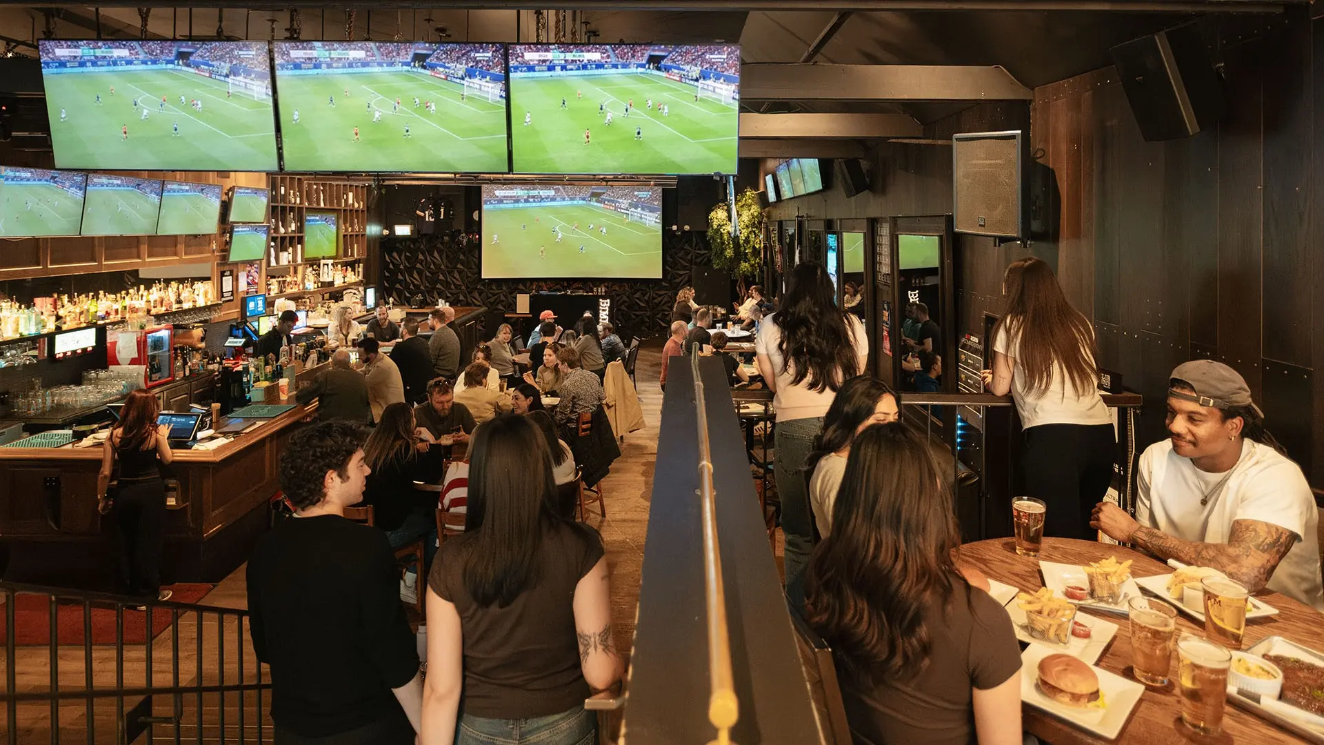 Crowded sports bar with people sitting at tables and bar, multiple TVs showing a soccer game.