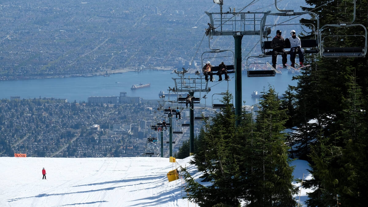 The ski lift at Grouse Mountain carries skiers up past a ski slope with the city of Vancouver in the background.