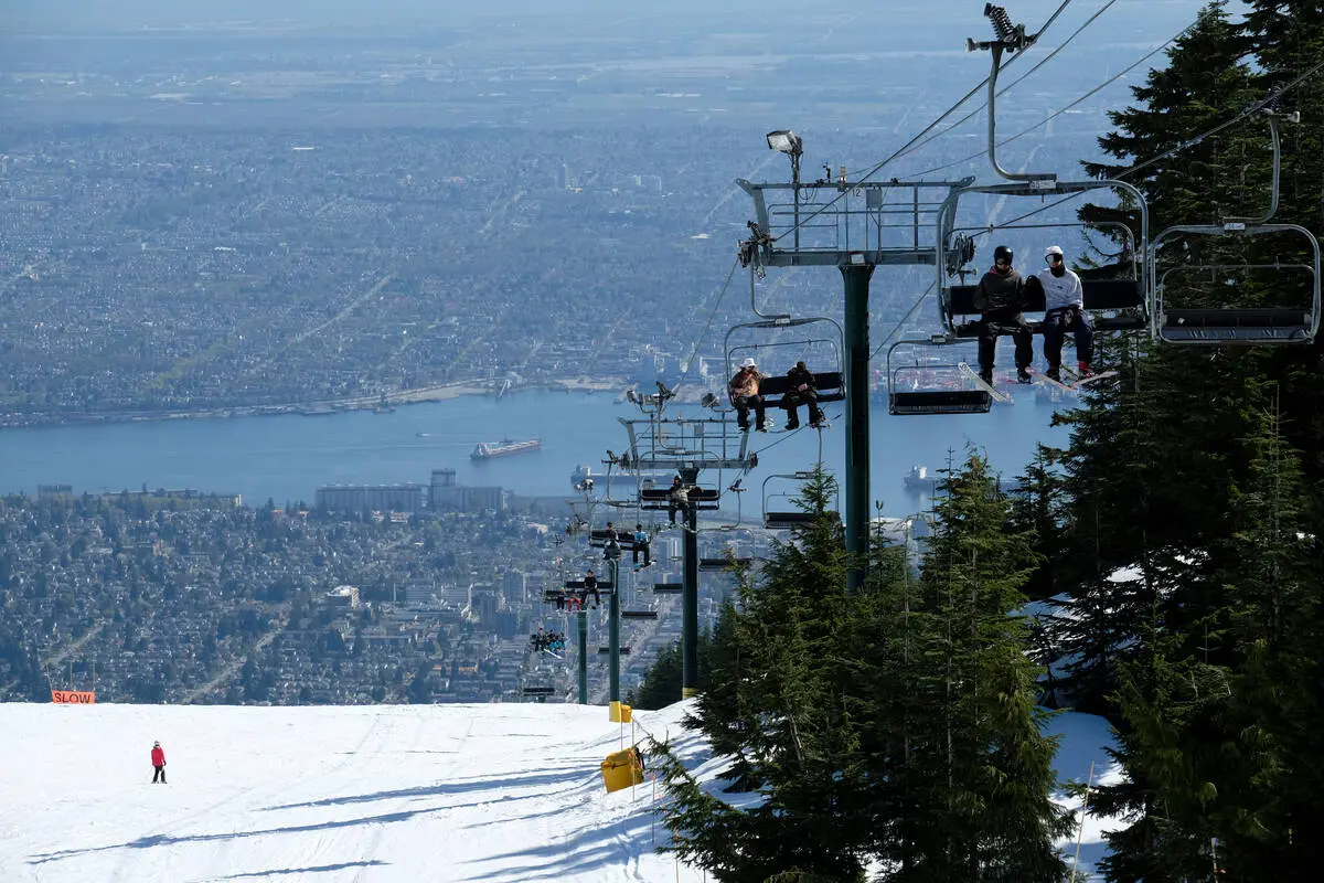 The ski lift at Grouse Mountain carries skiers up past a ski slope with the city of Vancouver in the background.