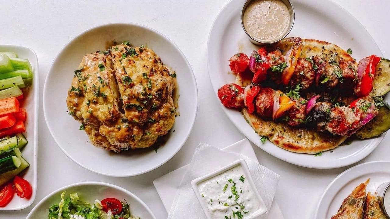 Greek food with Roasted Whole Cauliflower, Souvlaki Skewers, Tzatziki Sauce, and Salad and Vegetables