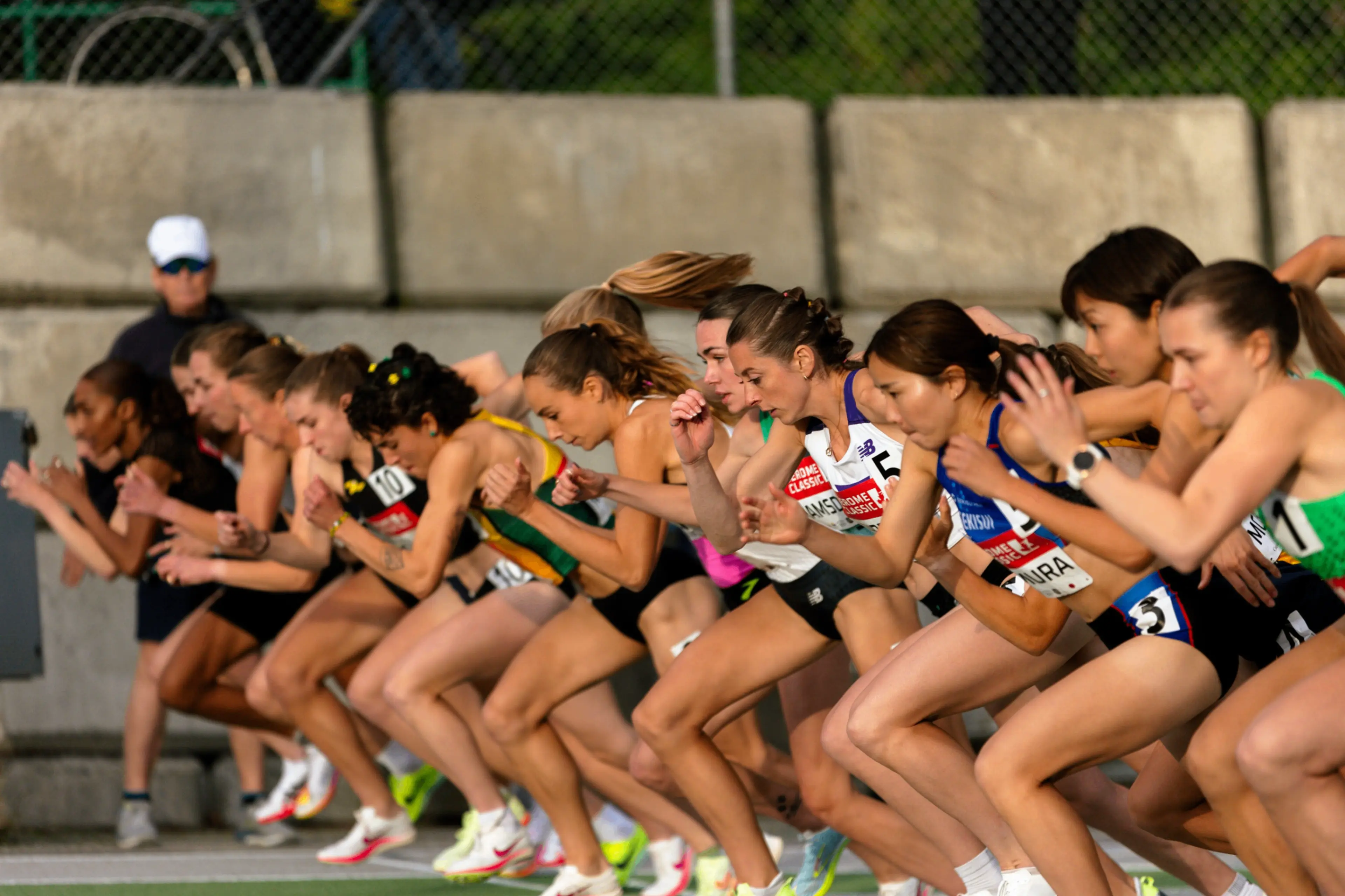 A group of female athletes in starting positions at the beginning of a race on an outdoor track.