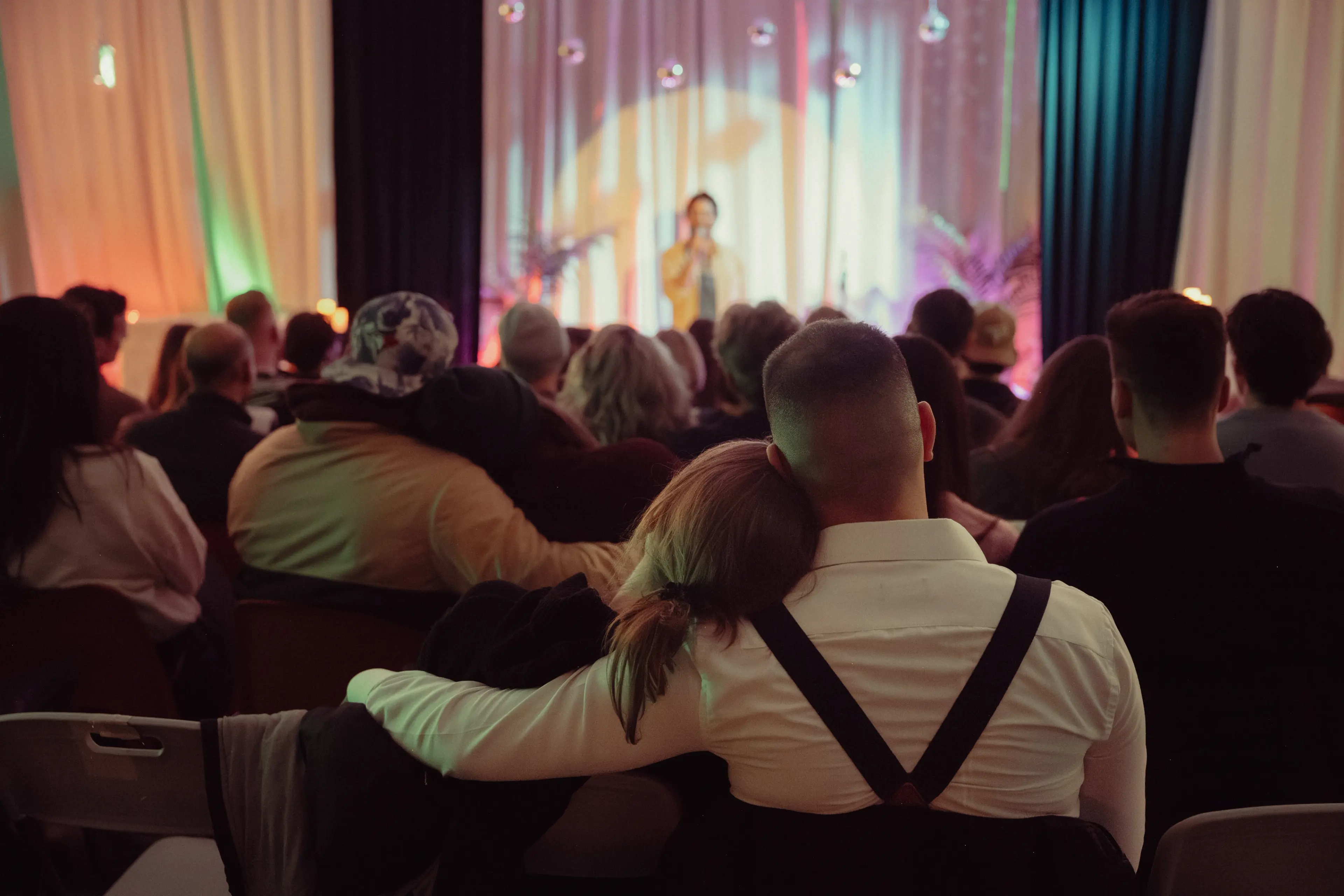 A couple with the partner having their arm around the other person both enjoying a show.