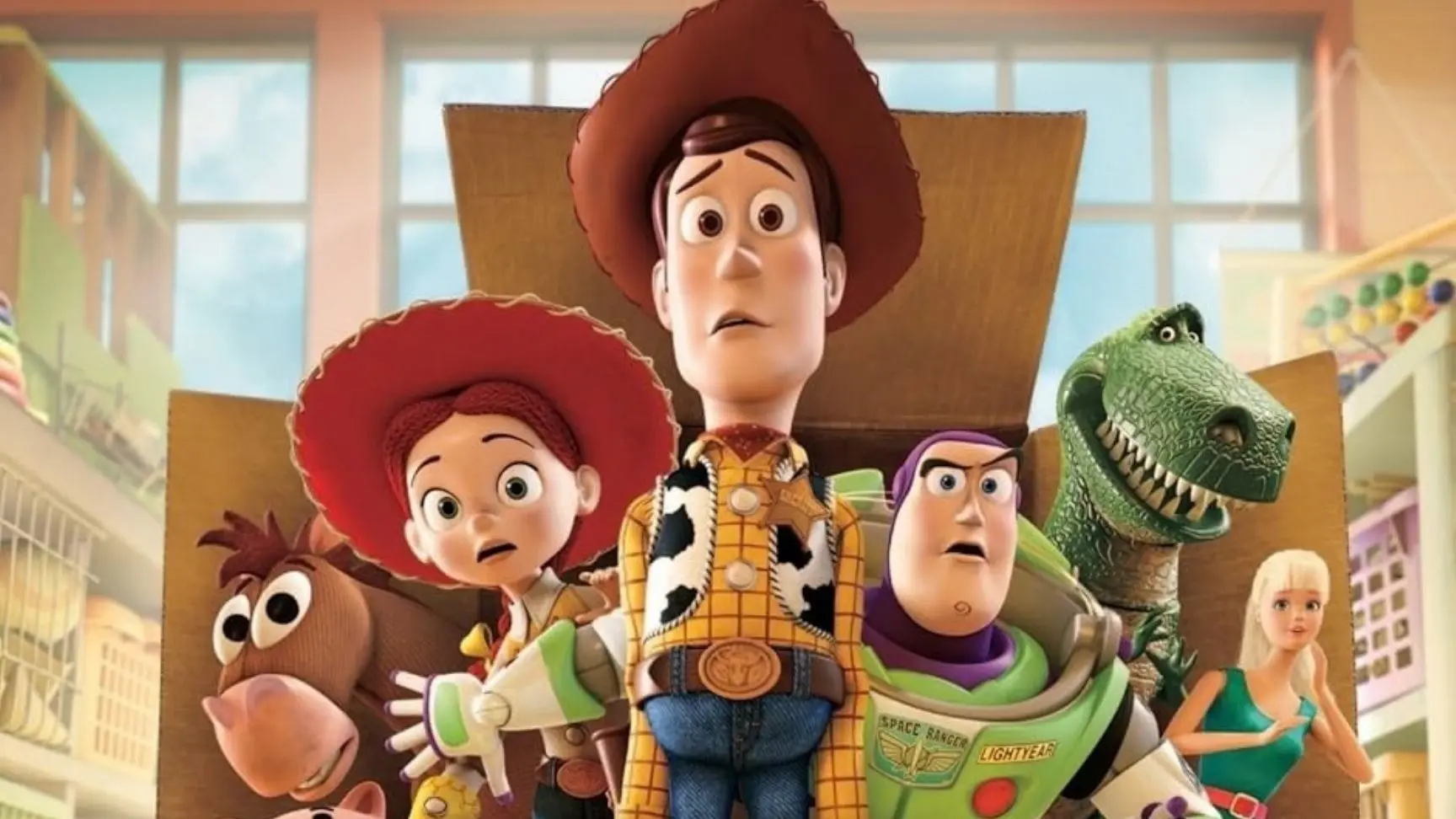 Animated characters Woody, Jessie, Buzz Lightyear, Rex, Bullseye, and Barbie standing inside a cardboard box in a room with large windows.
