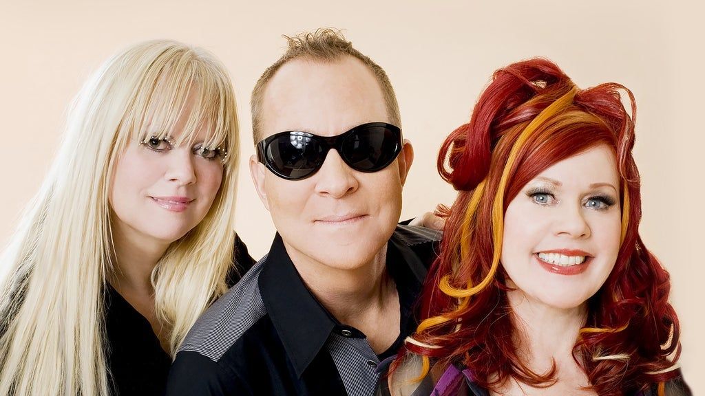 Three people posing together, one with long blonde hair, one wearing black sunglasses, and one with red and orange styled hair, all smiling.