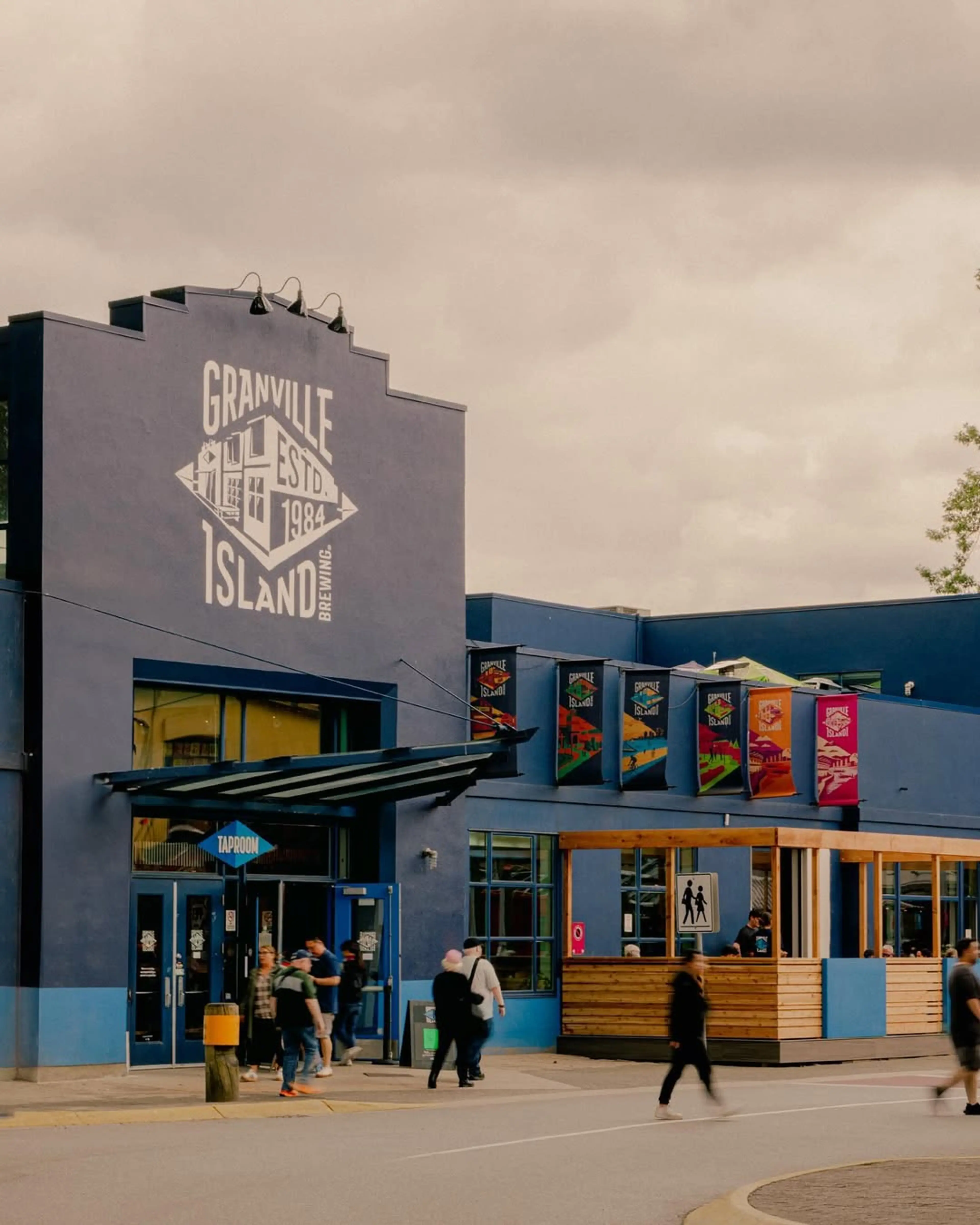 Blue building with Granville Island Brewing logo and people walking near the entrance under a cloudy sky.