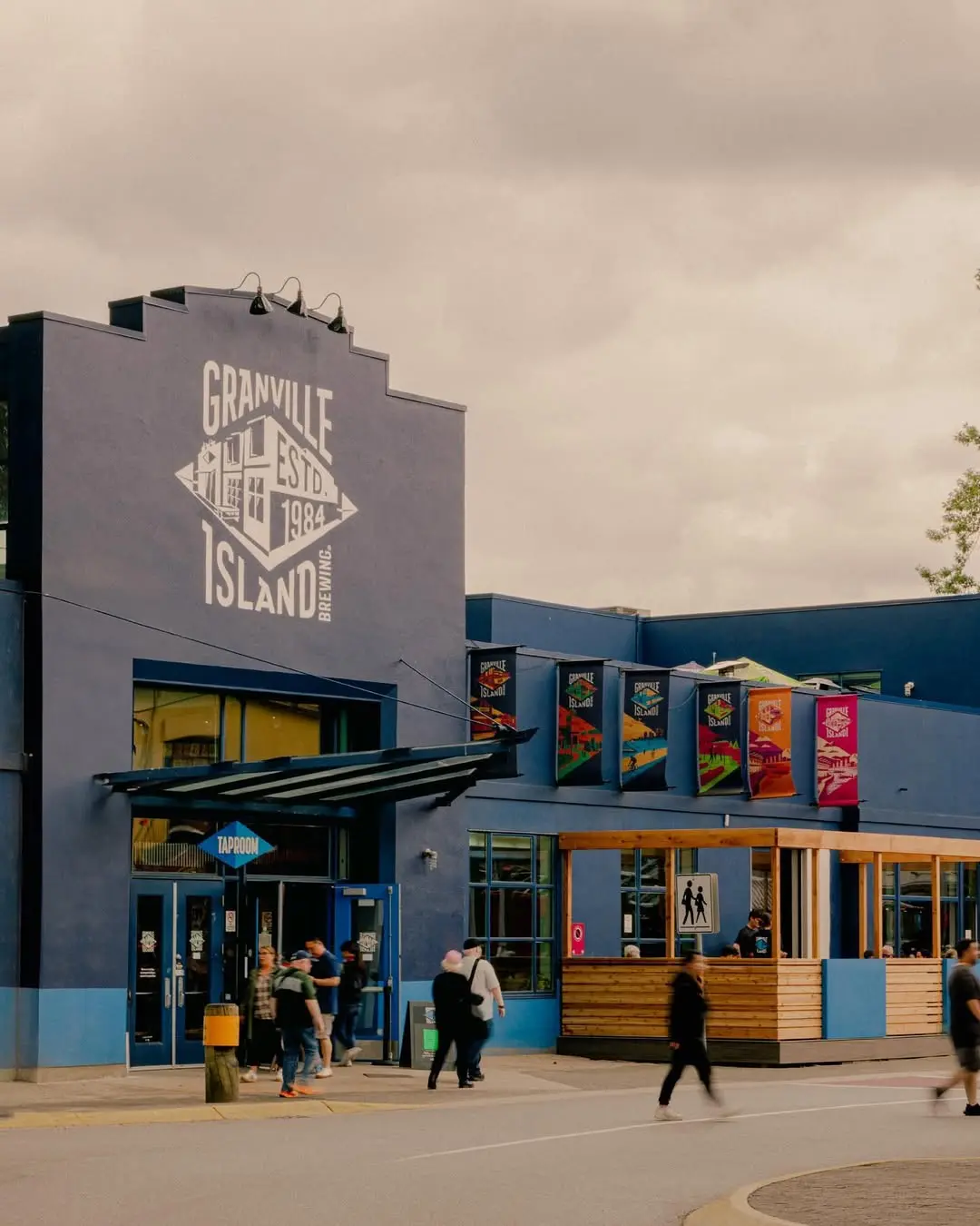 Blue building with Granville Island Brewing logo and people walking near the entrance under a cloudy sky.