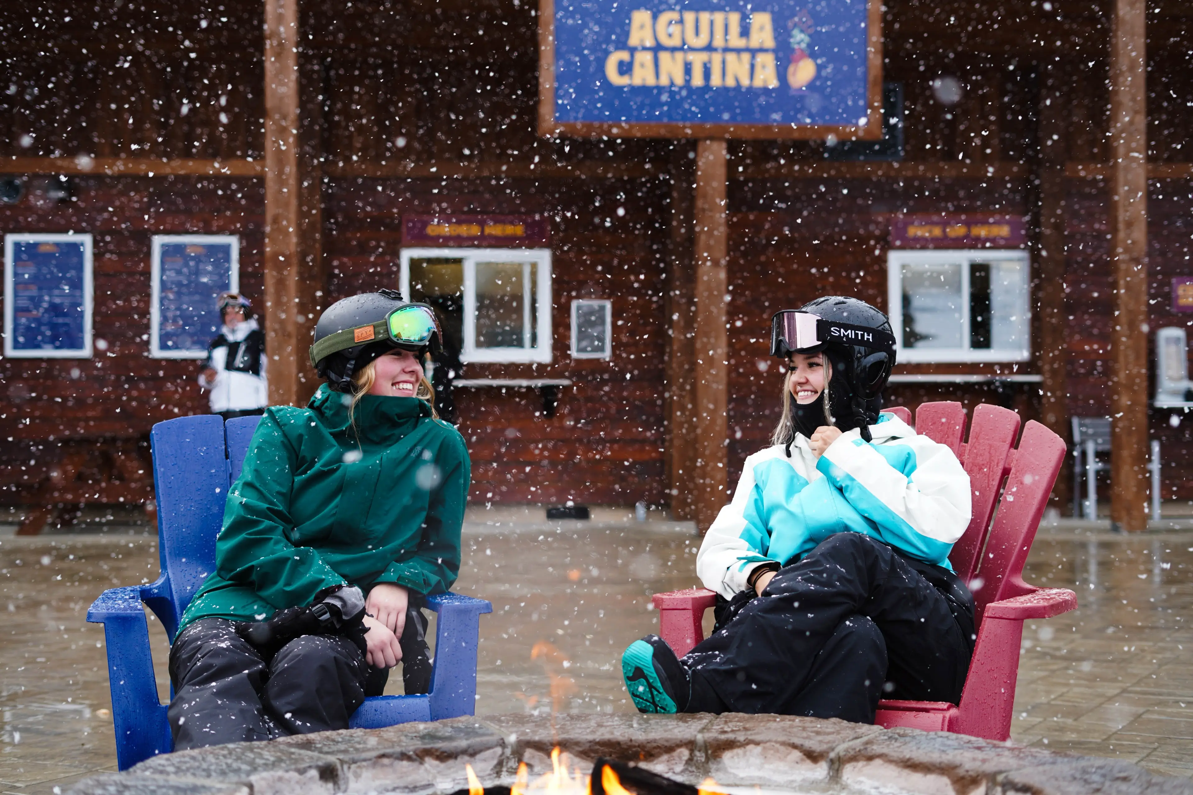Two women in ski gear sit on the patio at Cypress Mountain enjoying apres in the snow. 
