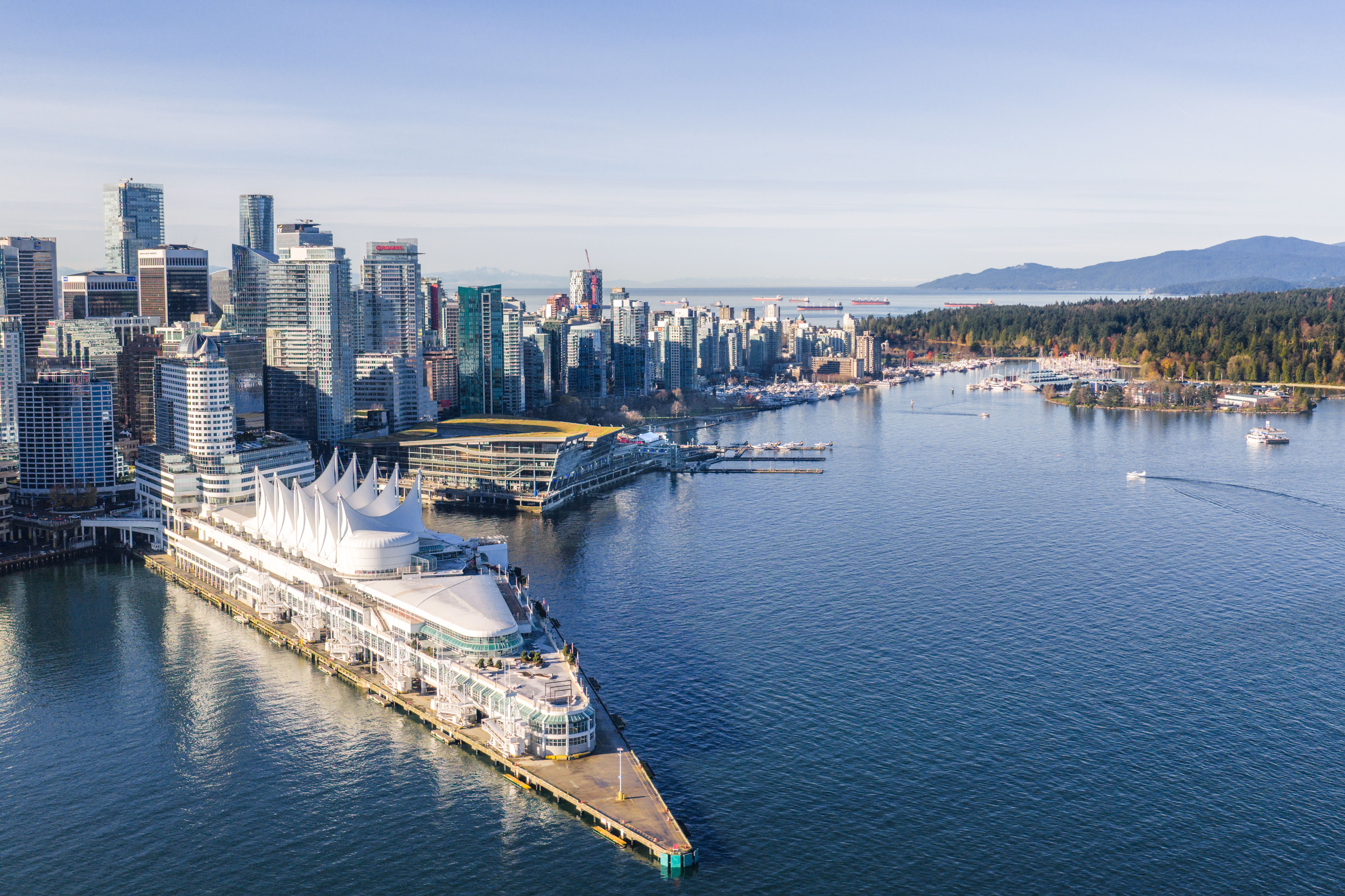 Aerial view of a waterfront city skyline with modern high-rise buildings and a large white tent-like structure on a pier extending into calm water.