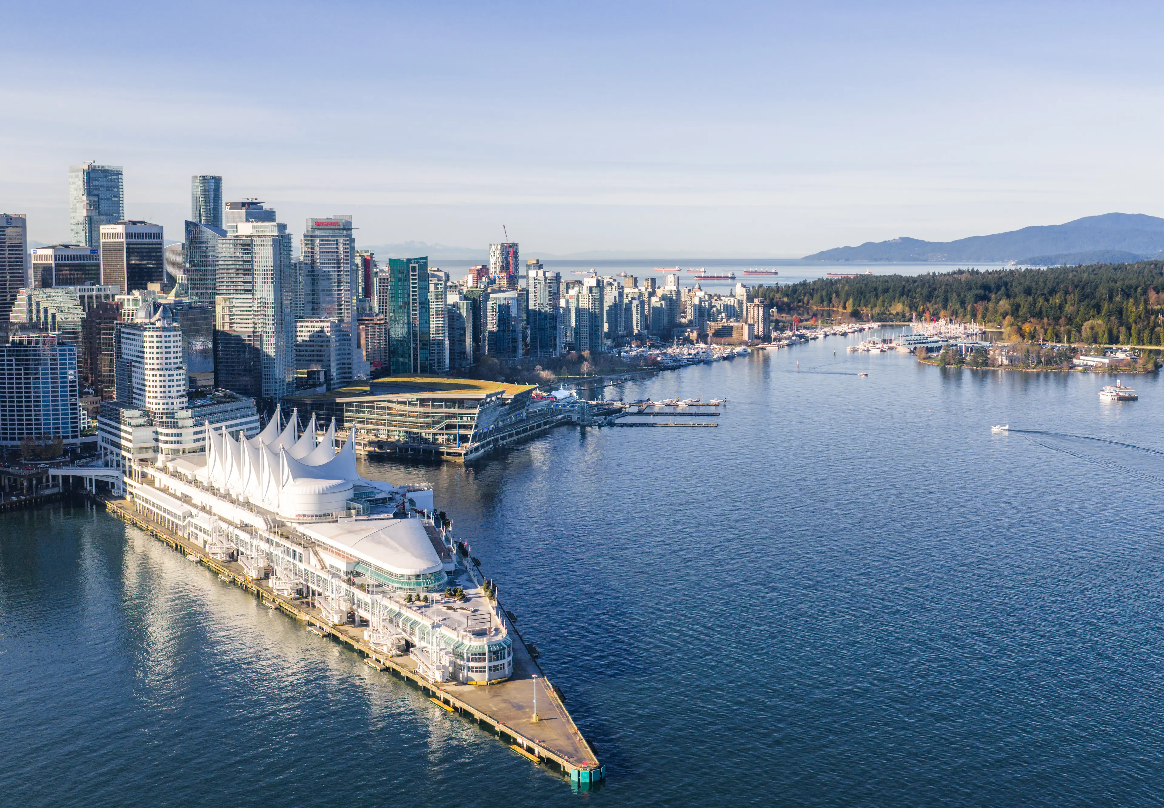 Aerial view of a waterfront city skyline with modern high-rise buildings and a large white tent-like structure on a pier extending into calm water.