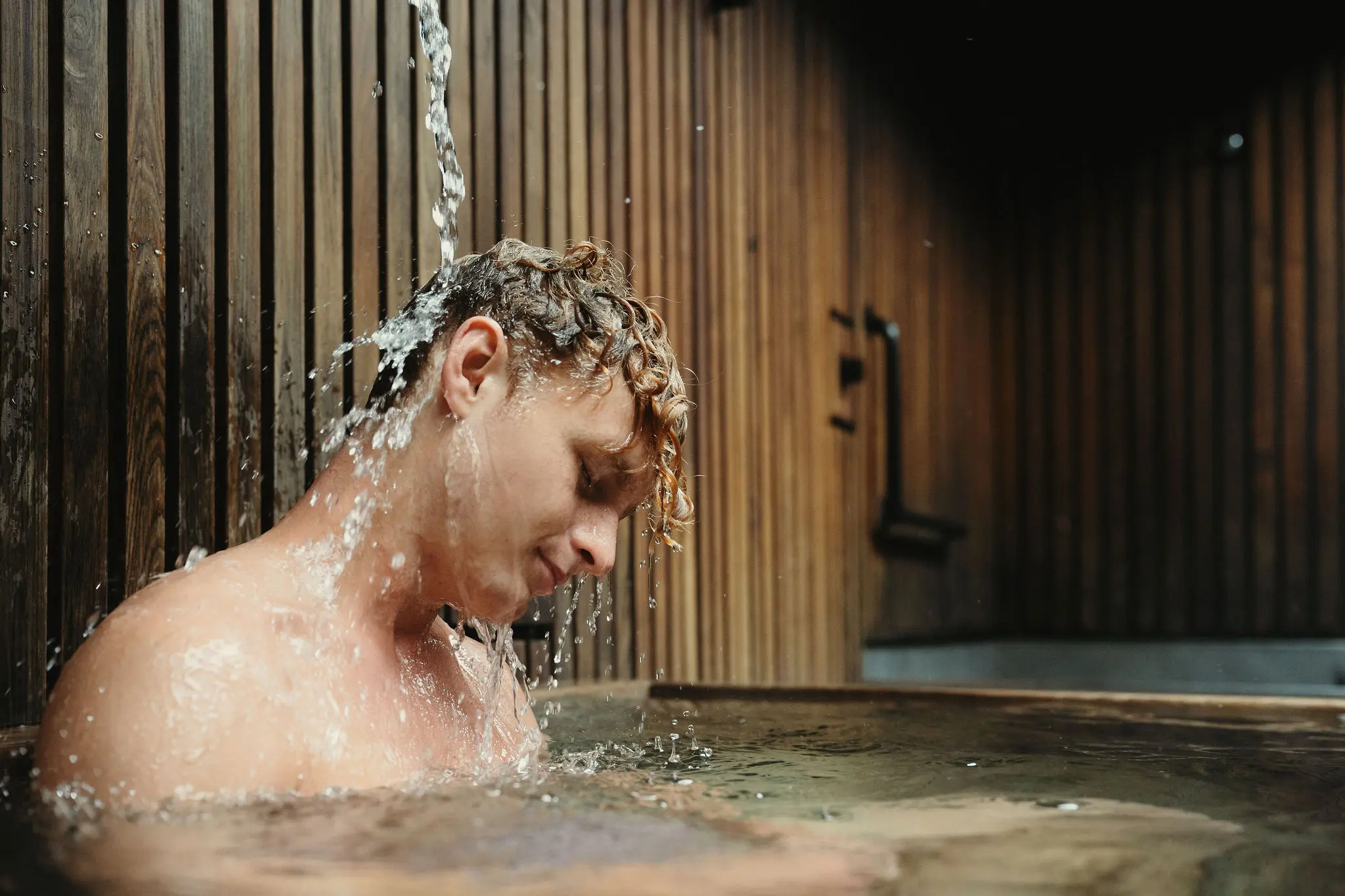 A person enjoying letting water run over their head at the Circle Wellness Spa at Granville Island, Vancouver.