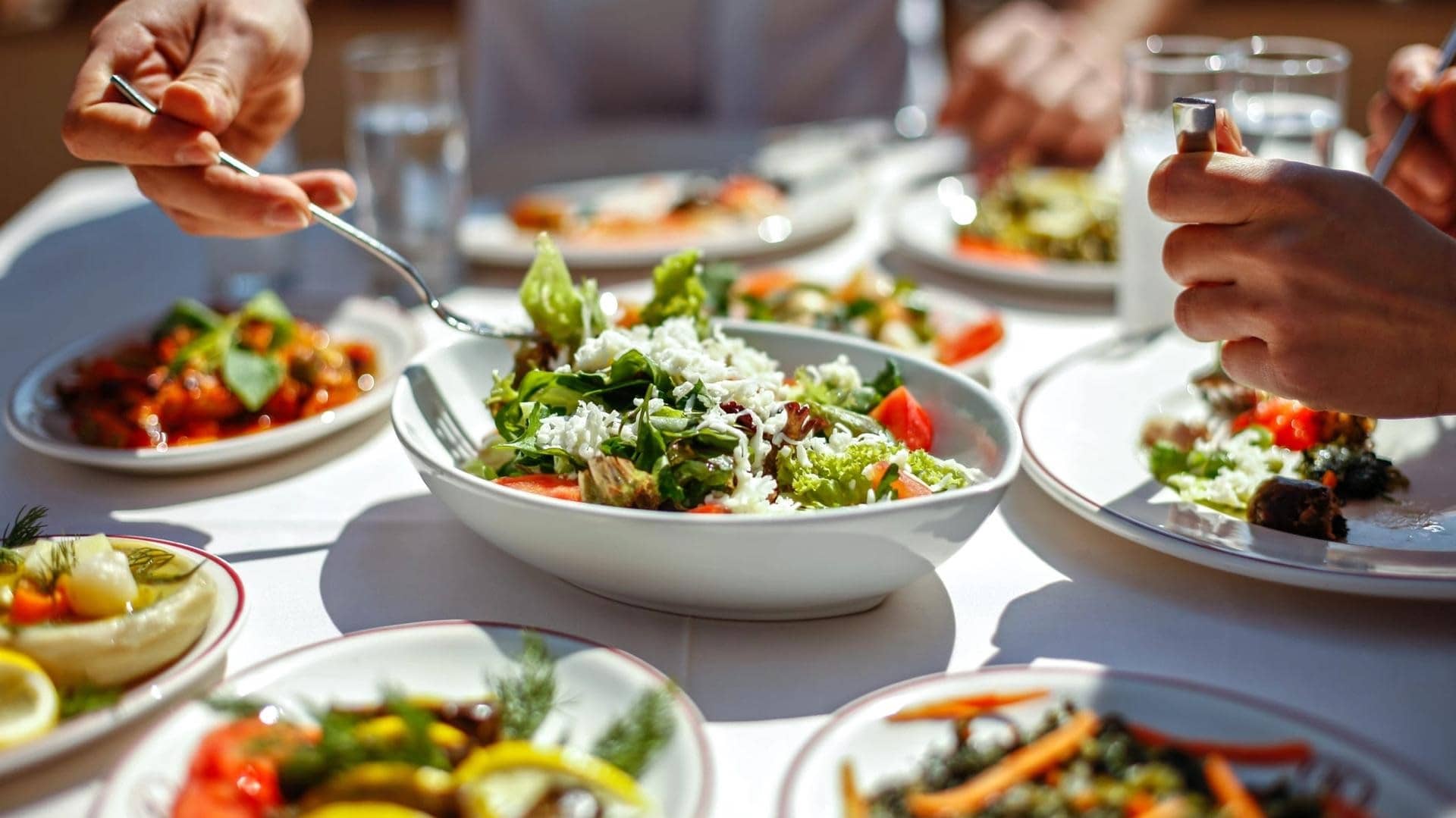 People are tasting a variety of salads on a table with white table cloth